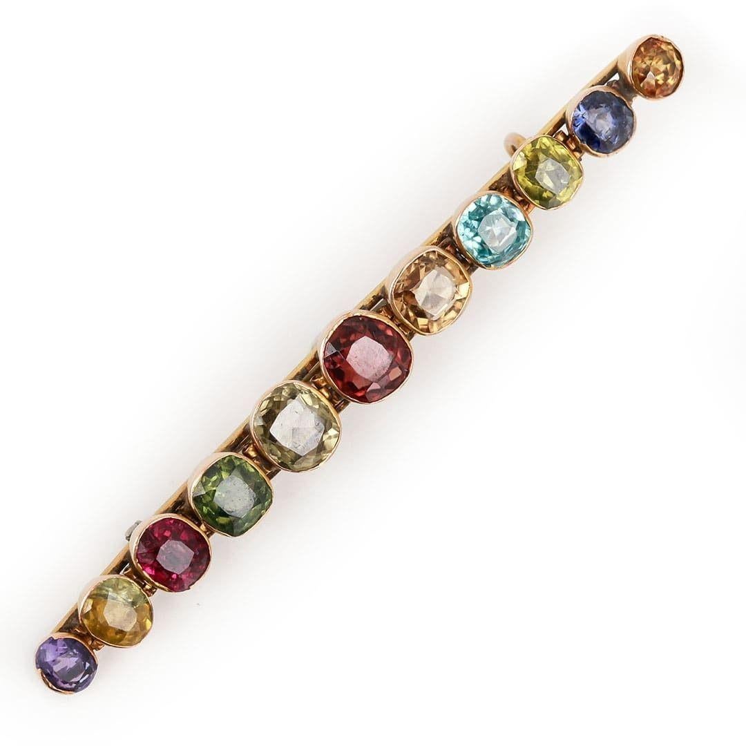 A fabulous and playful Edwardian ‘harlequin’ bar brooch dating from circa 1905. The 11 rub over set gemstones include deep red garnets, a muted green peridot, an electric light blue zircon, vary hue topaz, a lovely violet amethyst and a royal blue