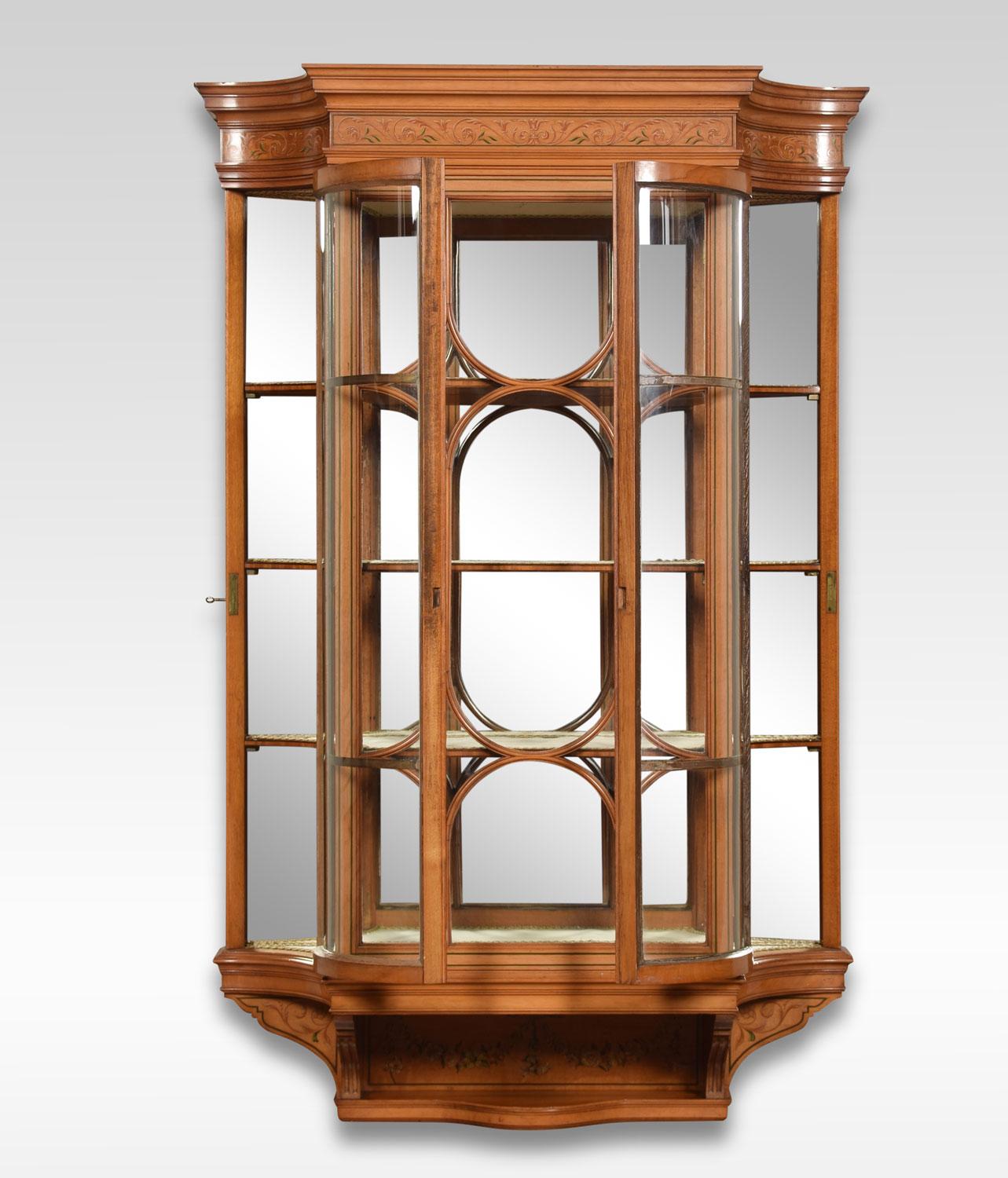 Edwardian painted satinwood wall hanging display cabinet, the stepped cornice above a foliate painted frieze and ribbed glass panel flanked by two unusual concave doors enclosing three shelves over a short, recessed, shelf and foliate swag painted