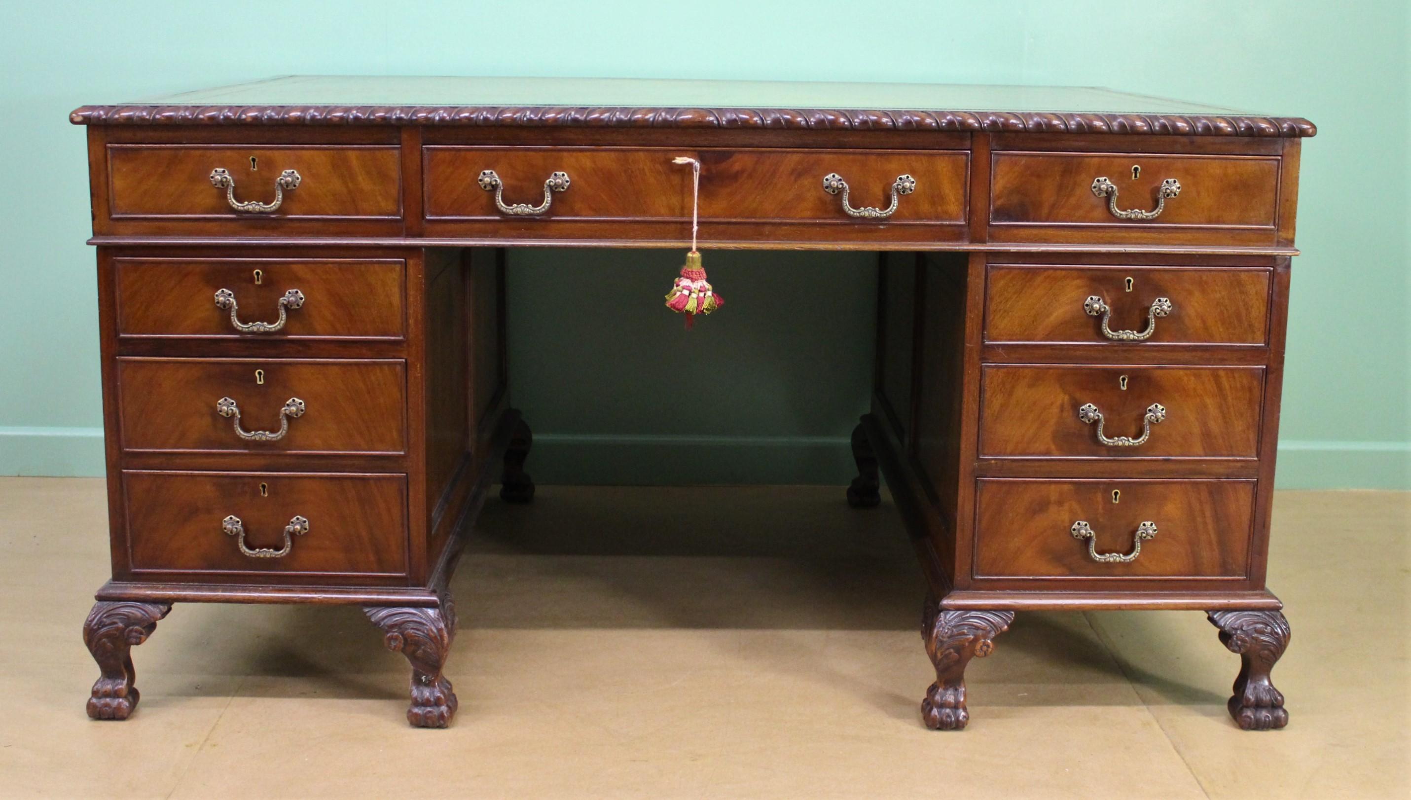 This marvellous and substantial Edwardian walnut partners desk is supported on 8 carved paw feet and features the original brass pull handles. The desk has a lovely colored green leather tooled top with a gadrooned mahogany edge. One side features 4