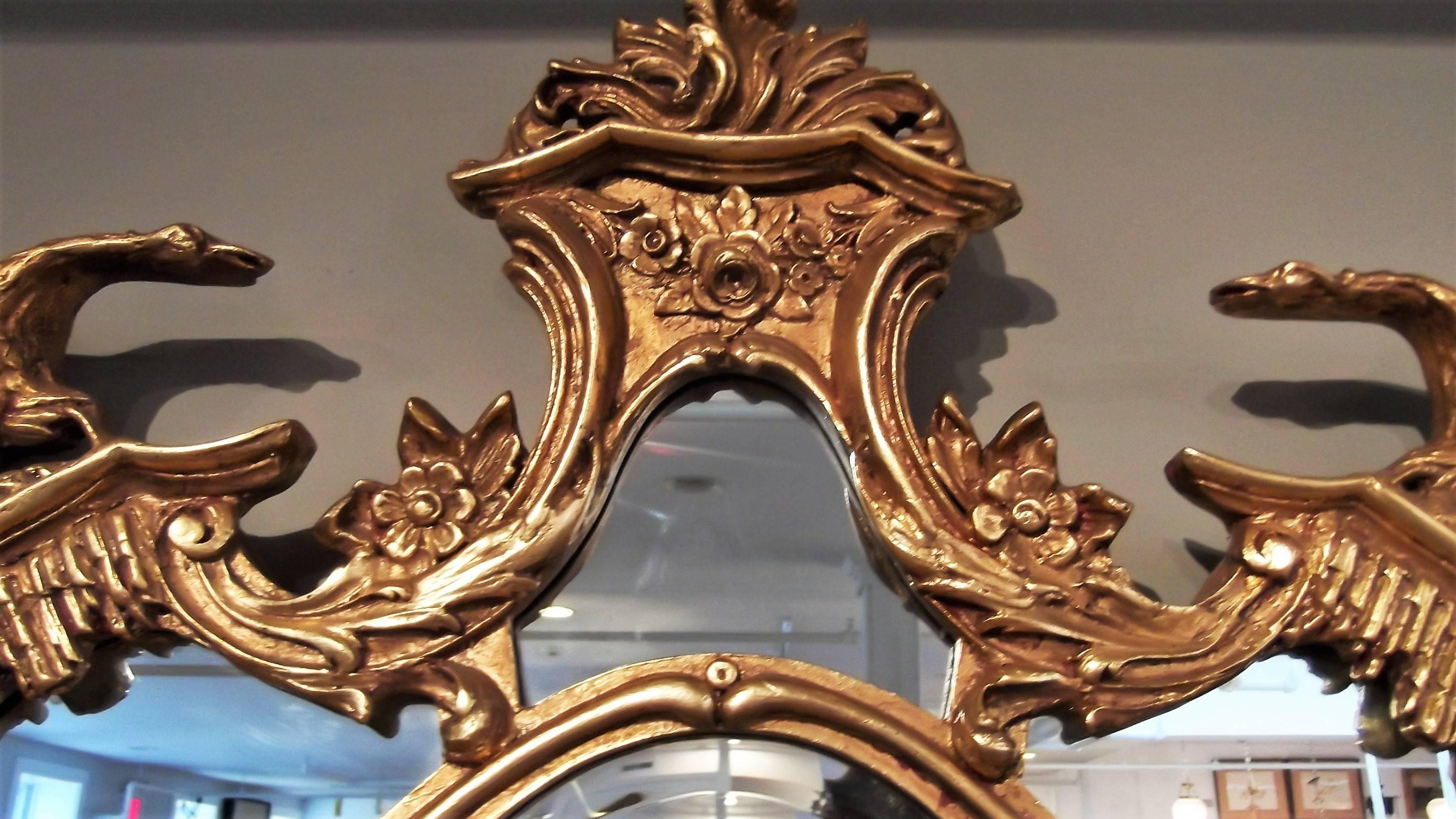 Elaborate framed giltwood mirror made by Friedman Brothers. A center plume top pediment flanked by a pair of swans with Rococo scrolls along the sides and bottom. Impressive size. The main portion of the mirror is beveled.