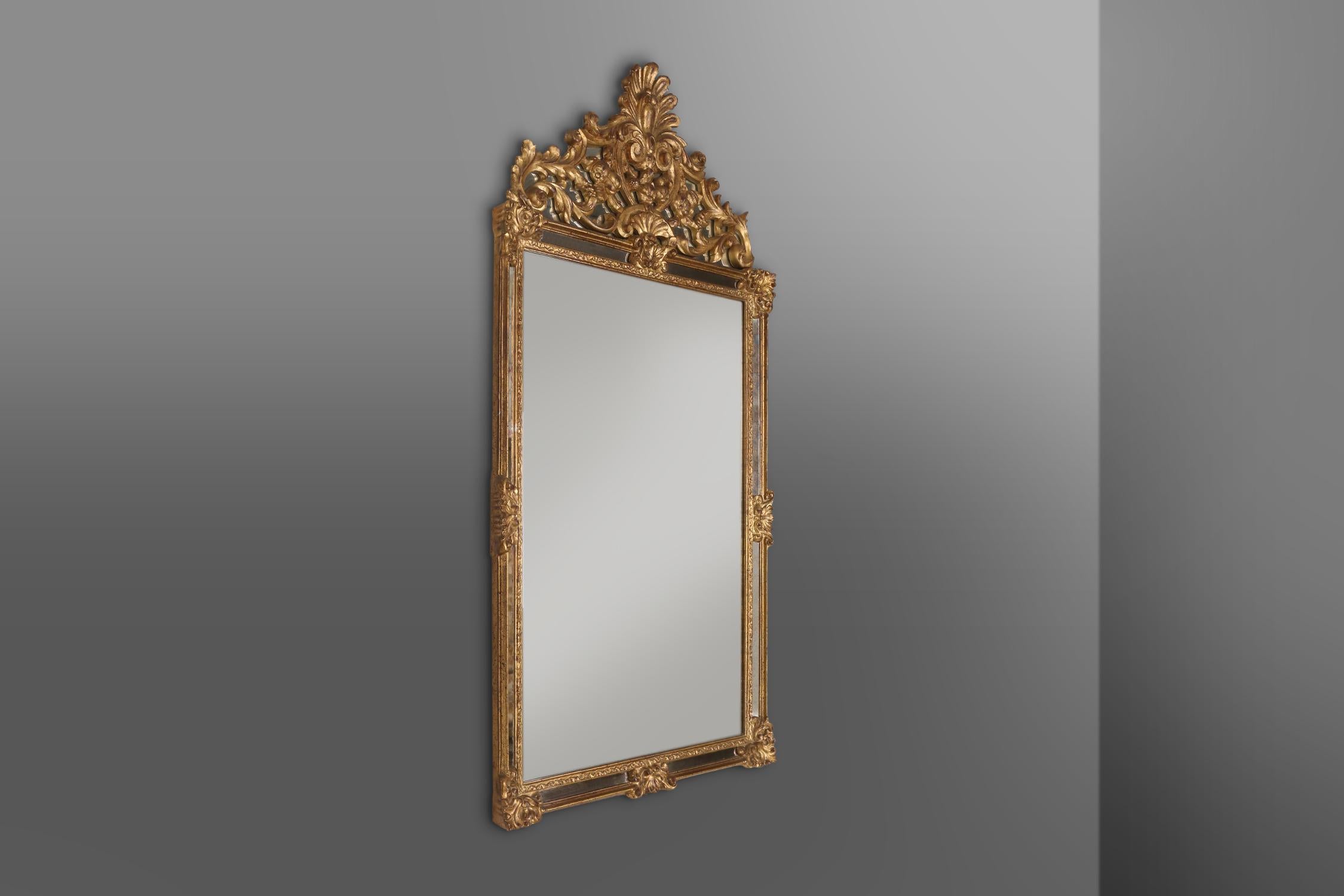 Large gilded mirror with romantic decorations and antique look. Made in Belgium by Deknudt in the seventies. The mirror has a rectangular resin frame with exquisite decorations and a spectacular top. On all sides the frame has smoked mirror glass