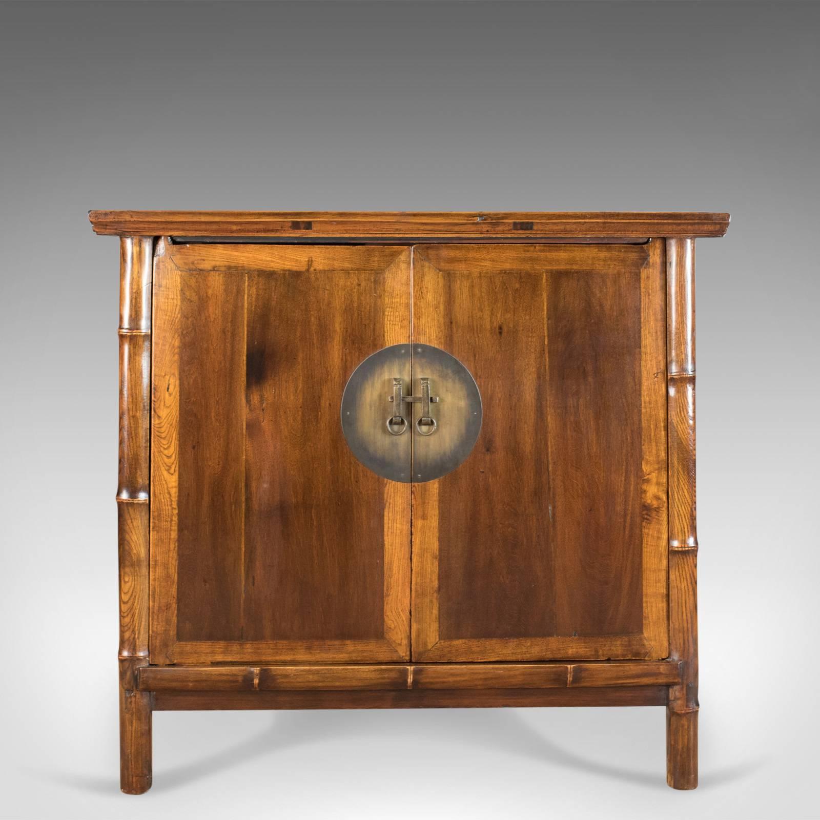This is a large elm cabinet in the oriental taste, a late 20th century Chinese cupboard.

Mellow caramel hues in a subtle two tone design
Attractive grain interest in the wax polished finish
Raised on circular section bamboo style legs