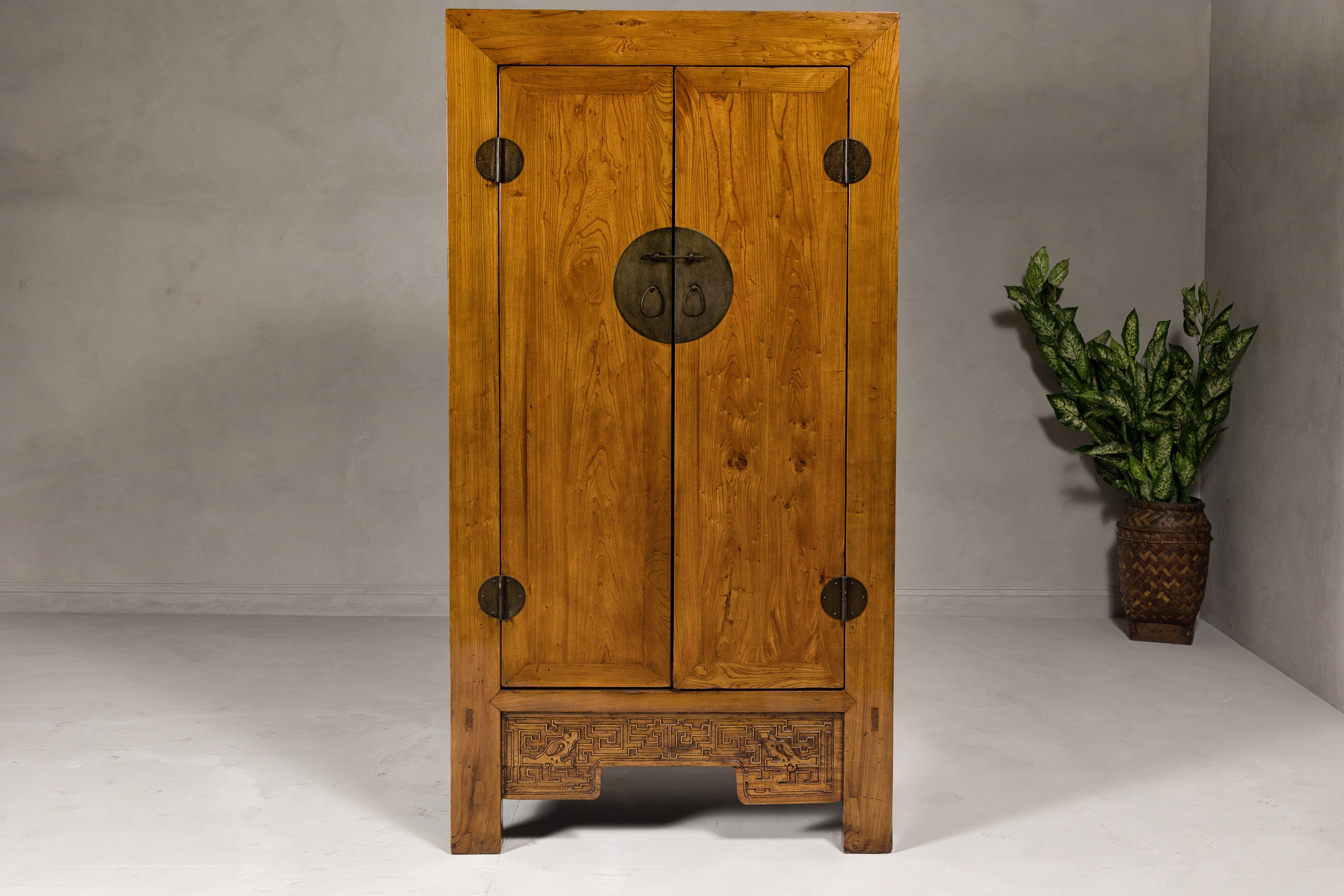 A large elmwood Qing Dynasty period cabinet from the 19th century with carved apron, round brass medallion hardware and two doors. This exquisite large elmwood cabinet, hailing from the Qing Dynasty period of the 19th century, is a masterpiece of