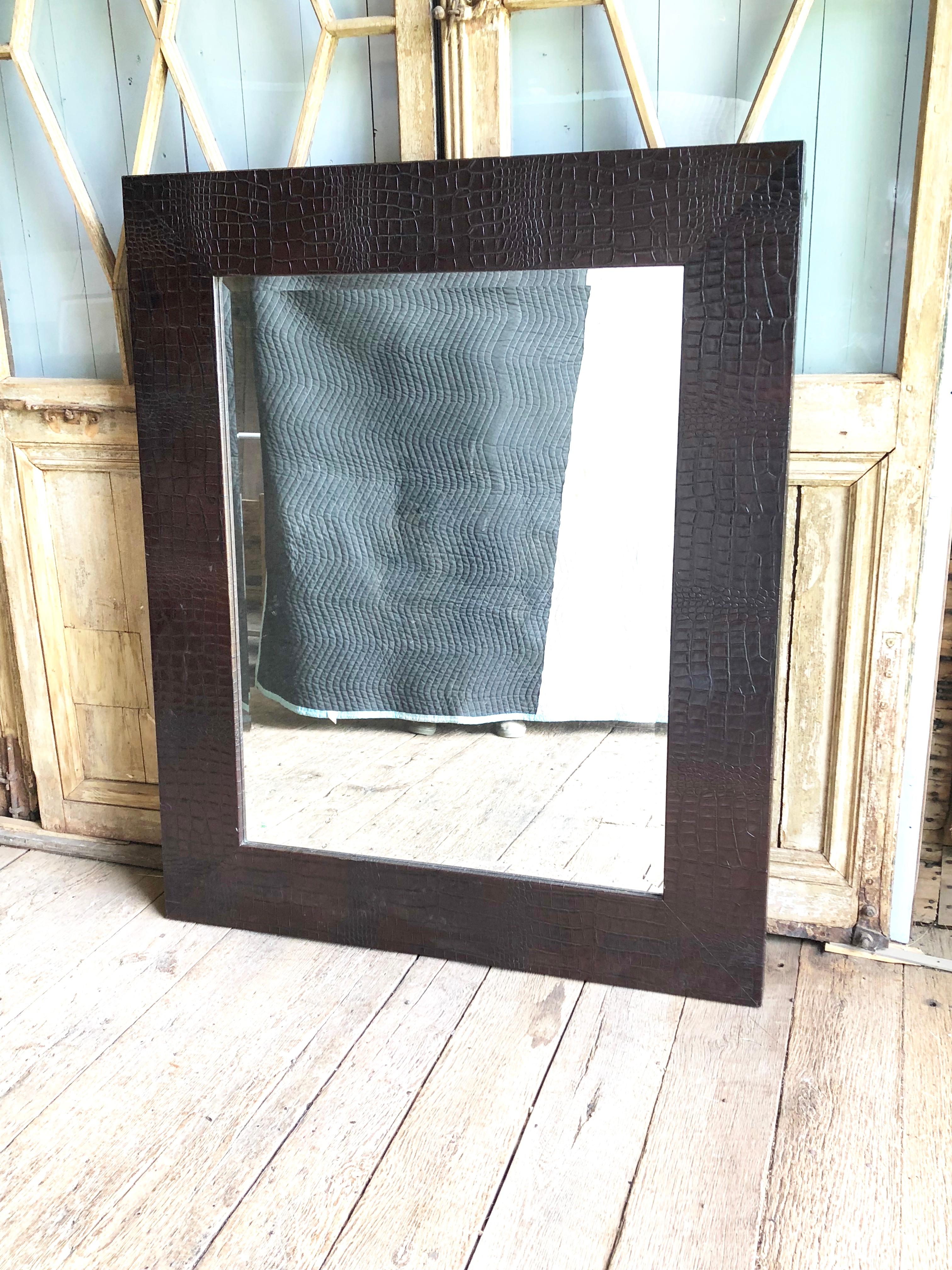 A large wall mirror with heavy beveled-glass plate in a faux alligator embossed leather frame.