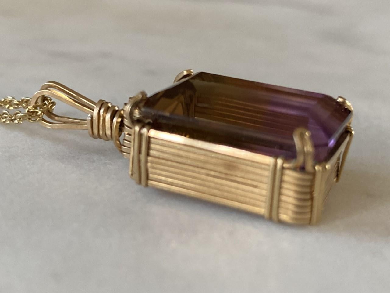 Crafted in the 1950s from 14kt yellow gold, this vintage necklace features a large emerald-cut purple ametrine (a combination of an amethyst and a citrine) pendant measuring 20mm x 15mm. The chain measures 18 inches long. The ametrine is encased in