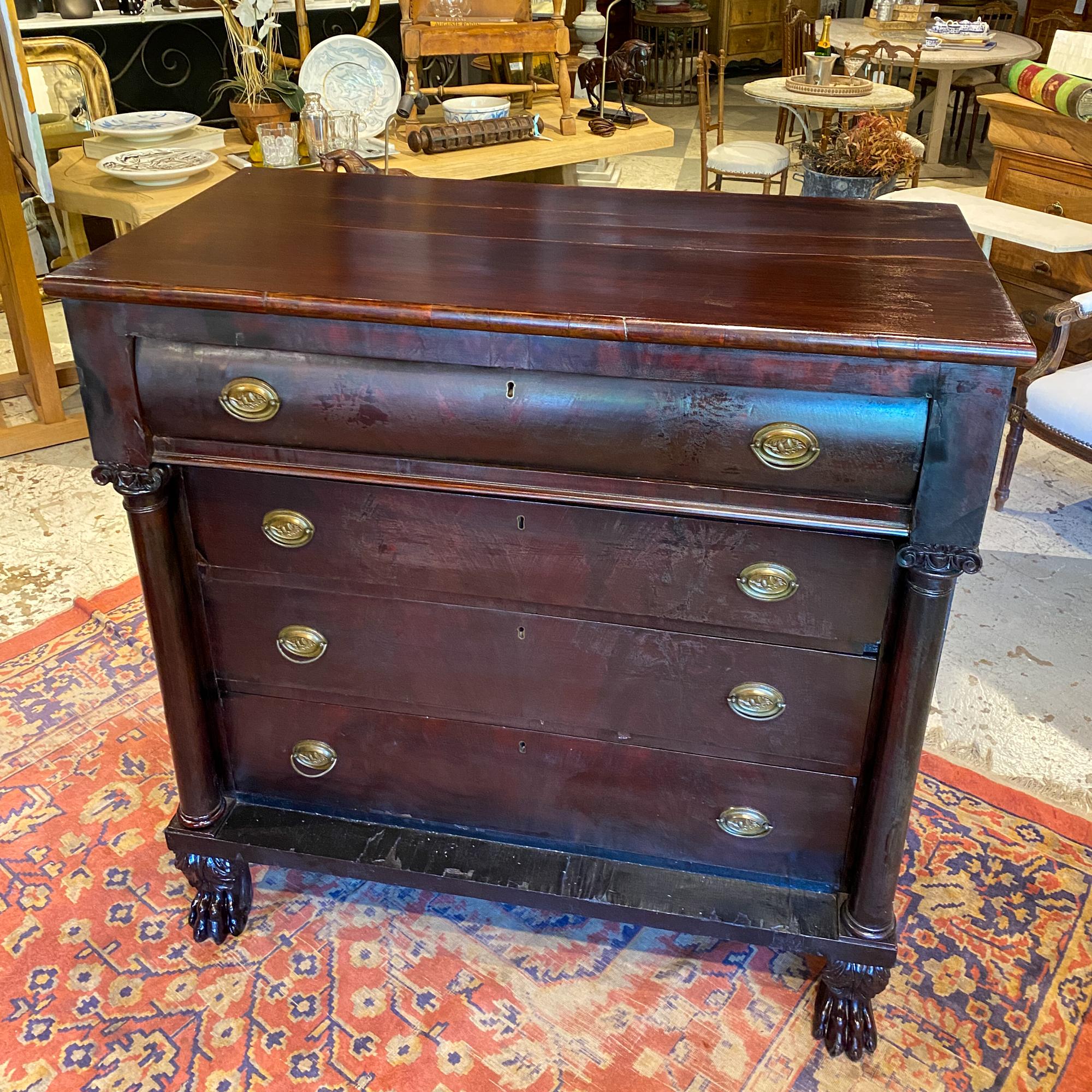 This stately Empire style chest of drawers features ornately carved paw feet at the front, four generous drawers, pillar details and brass hardware. The oval-shaped brass bail pulls have thistle decorations cast into the bail plate. Each drawer has