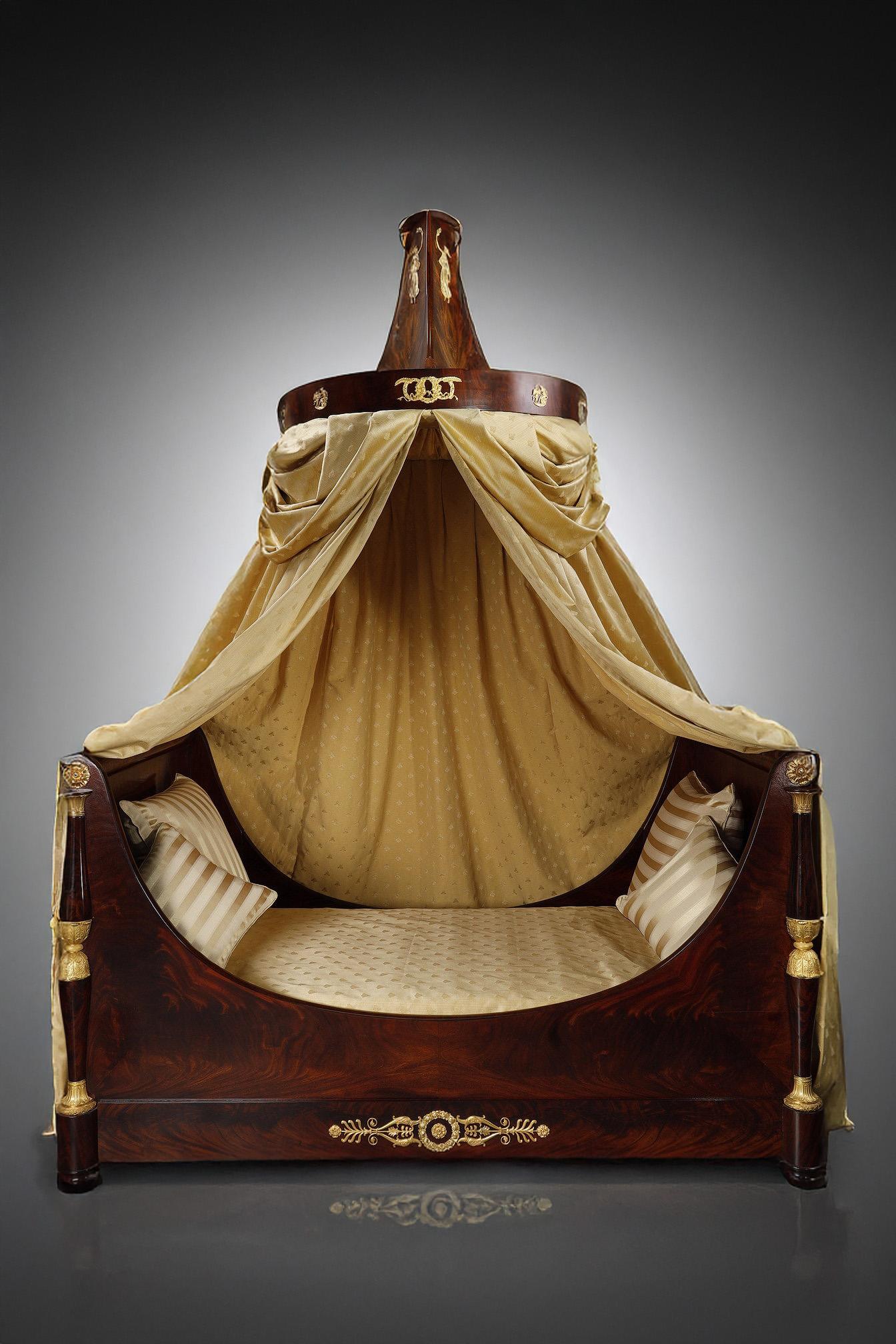 Large boat bed in solid flamed mahogany, mahogany veneer, richly decorated with finely chased and gilded bronzes, from the Empire period. Four baluster jambs, adorned with fleurons, acanthus leaves and palmettes, support the unit. On the front, both