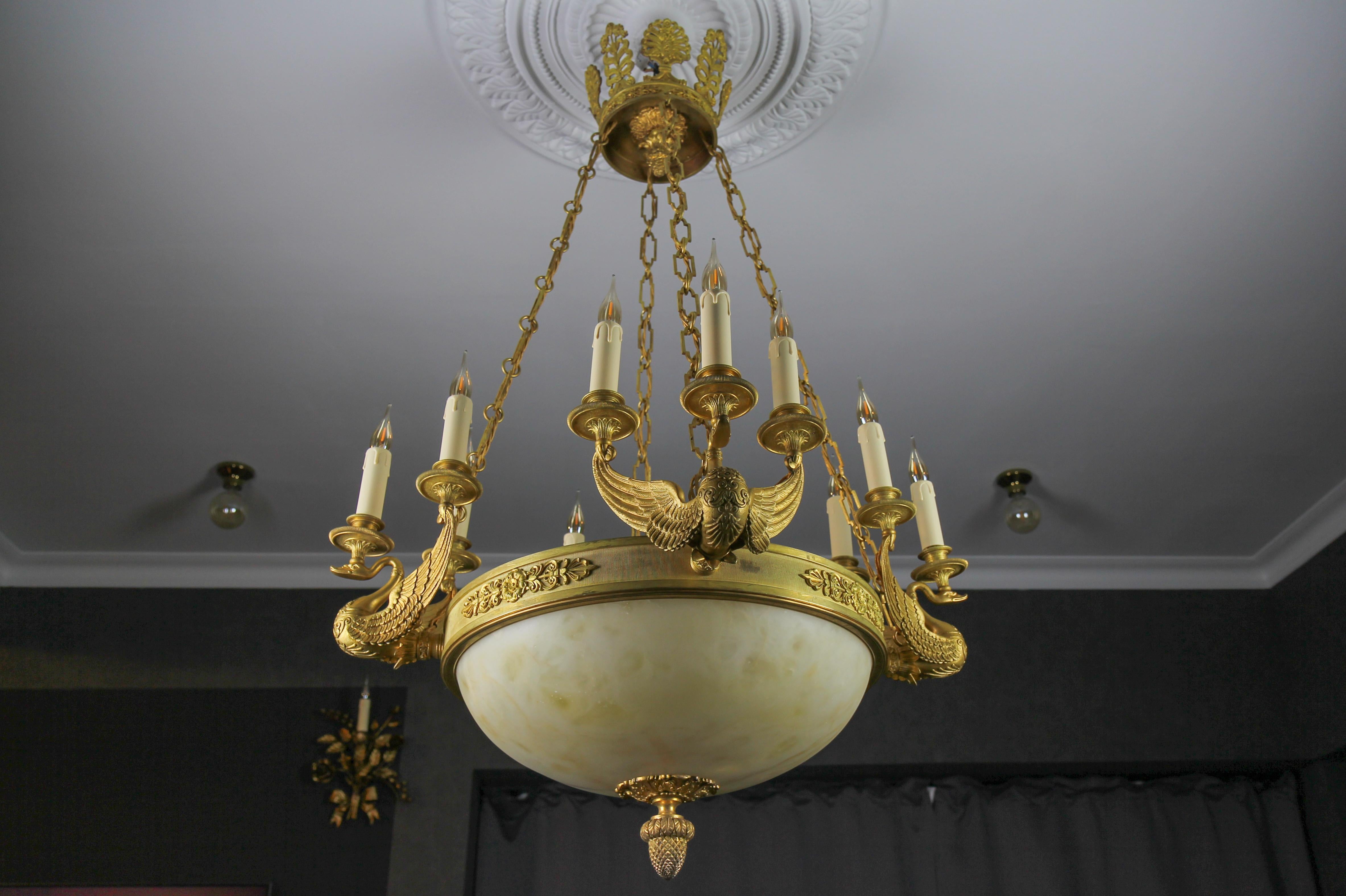 Magnificent and impressive Empire-style bronze and alabaster sixteen-light chandelier from the late 19th century; later has been electrified. The circular ring with four large majestic finely cast swan branches each supporting three lights with