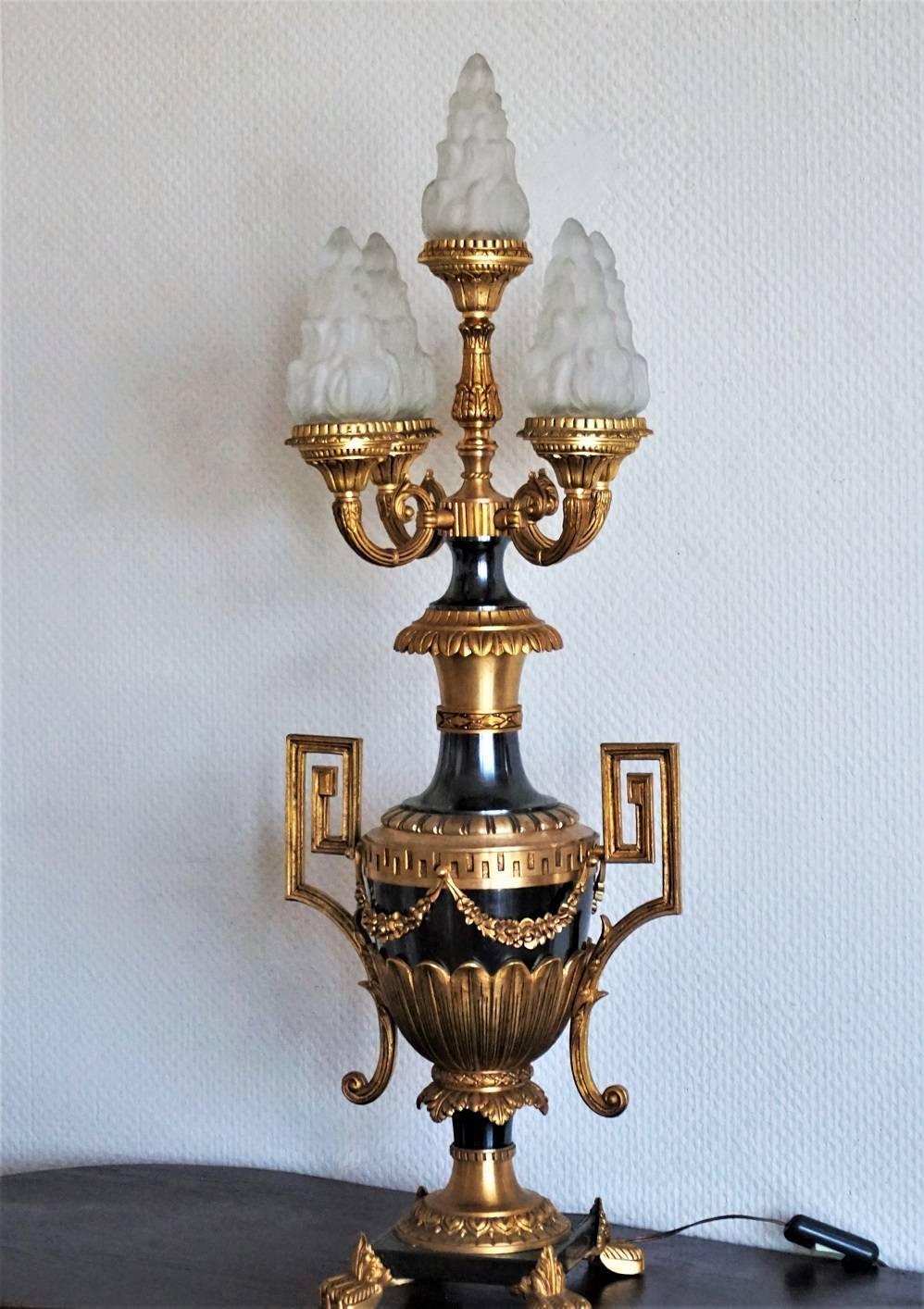 Large, heavy Empire style gilt and patinated bronze Amphora table lamp decorated with fine ornaments and garlands on a square base supported by four feet covered with leaves. Five-light with frosted glass flame shades.

Measures: Height: 33 in (83.5