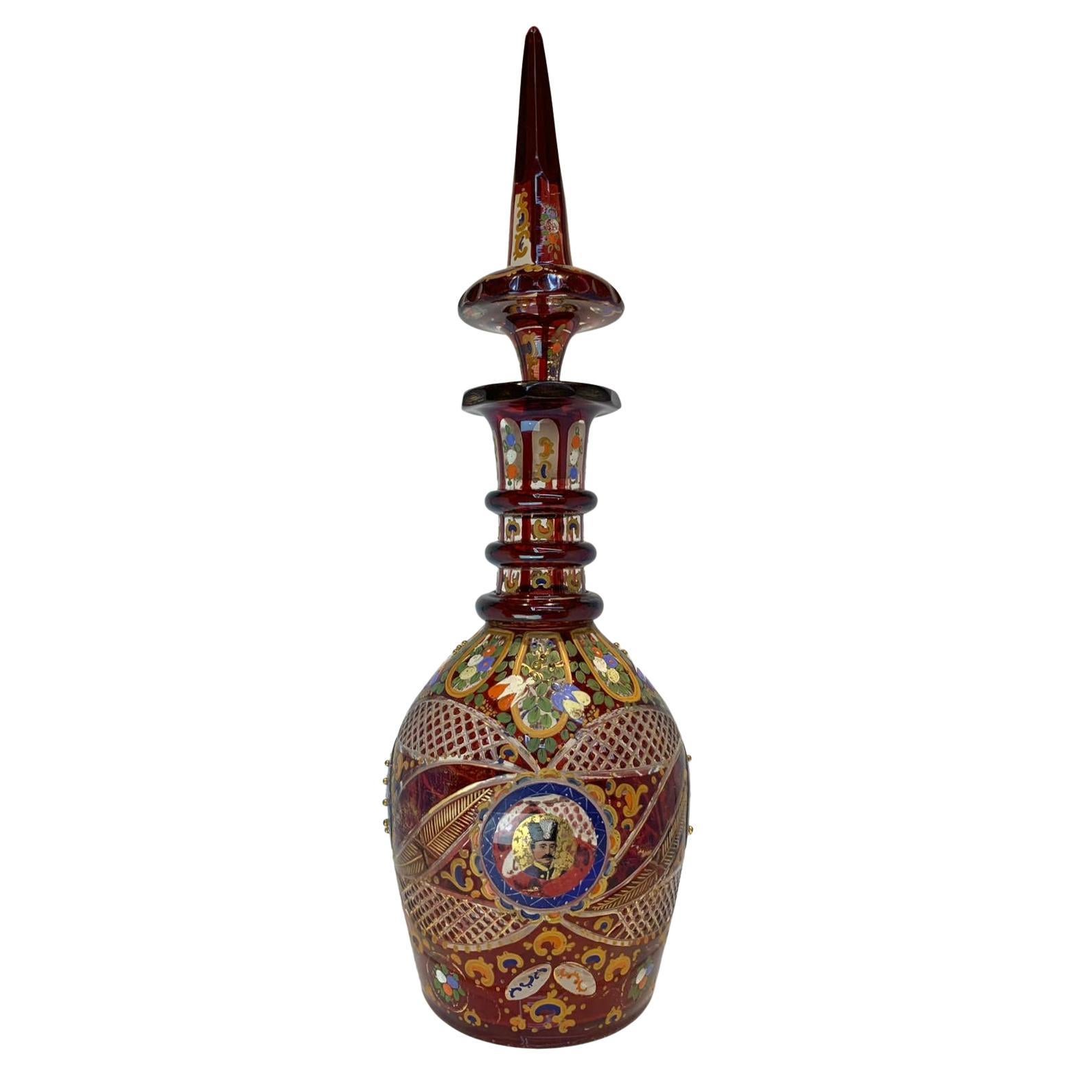 LARGE ENAMELLED GUT GLASS DECANTER
BOHEMIAN FOR THE PERSIAN MARKET

Enamelled with scrolls and bouquets and heightened in gilt
Decorated with glass beads
The sides with two royal portraits of an Iranian Shah

Height 53 cm
