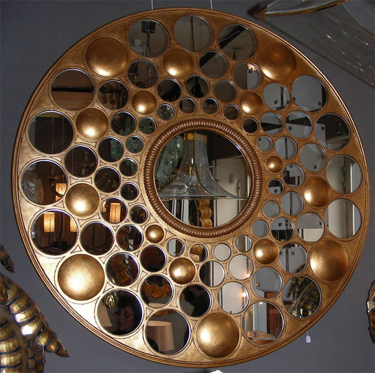 Miroir rond en bois doré.
Le cadre est percé de nombreuses fenêtres rondes sur quatre rangs,
chaque rangée contient de petits miroirs ronds de différentes tailles, parfois séparés les uns des autres de façon aléatoire par un macaron en bois doré,