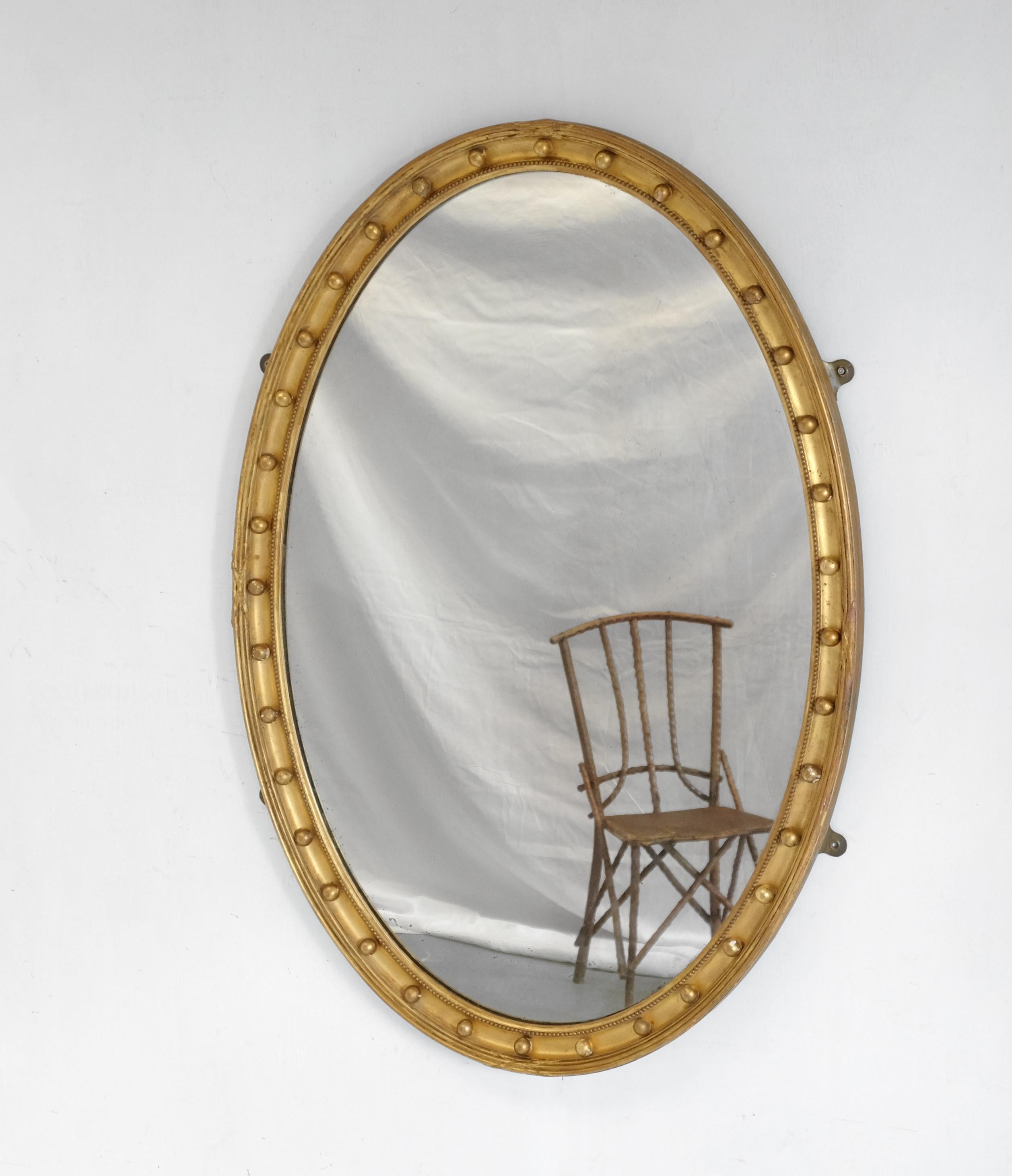 A large oval wall mirror in the Regency style. The giltwood frame with ribbon-tied reeding above a sphere filled cavetto. With original plate and backboards. Some light foxing and age-related fading to the glass. Can be hung portrait or landscape.