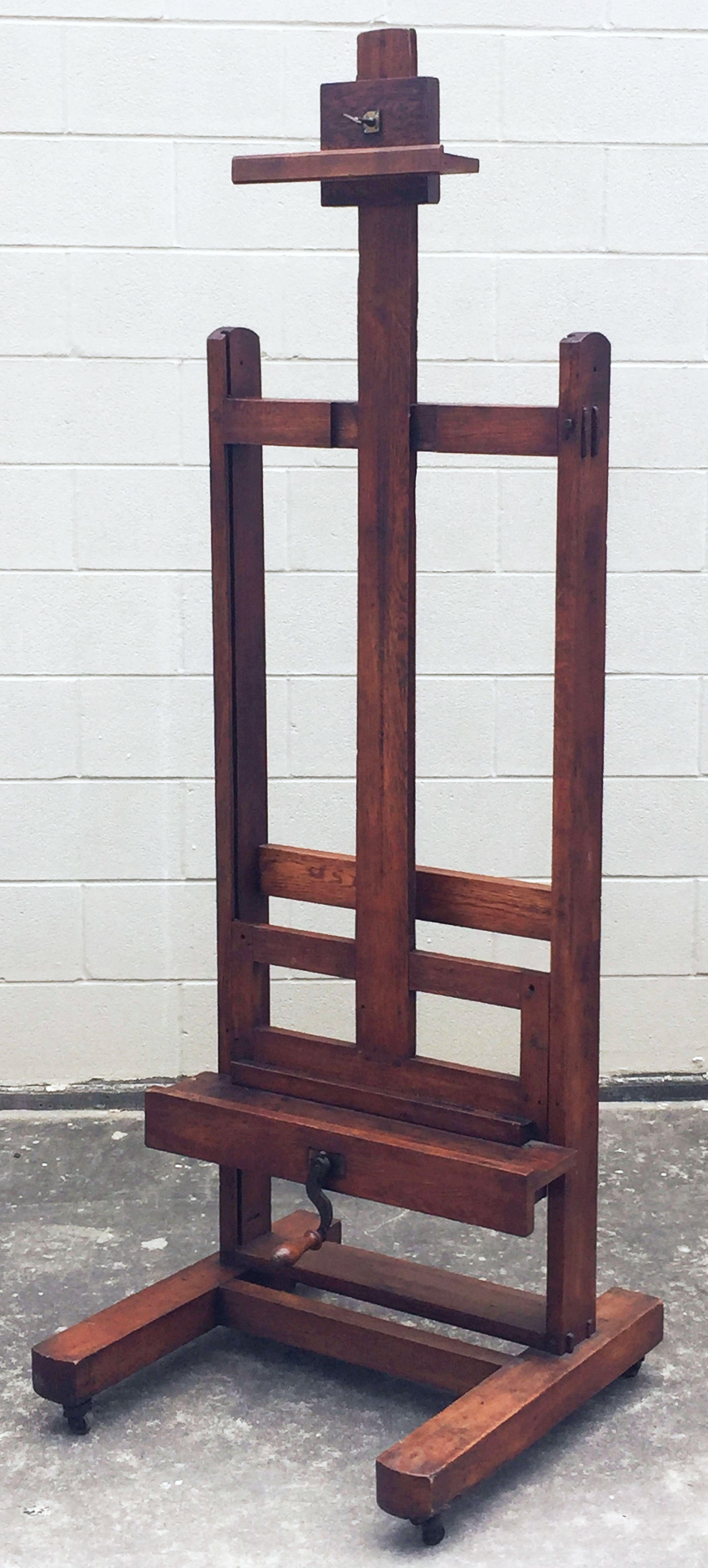 A handsome English artist's display or studio floor easel from the early 20th century, featuring a functioning crank mechanism to adjust the tray height, solid beam construction, on rolling casters. 

With an adjustable height of 73 inches to 102
