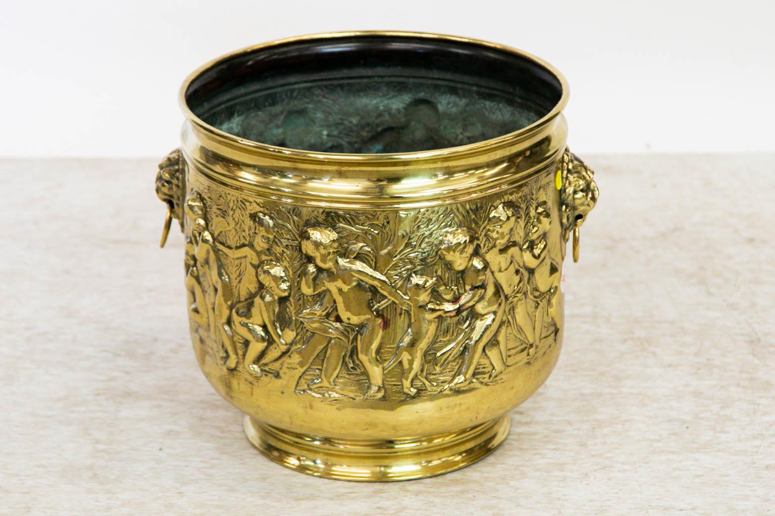 This brass can has large raised lion head pulls on the sides. There are raised allegorical and cupidlike figures in high relief. It has been polished and lacquered for ease of maintenance.