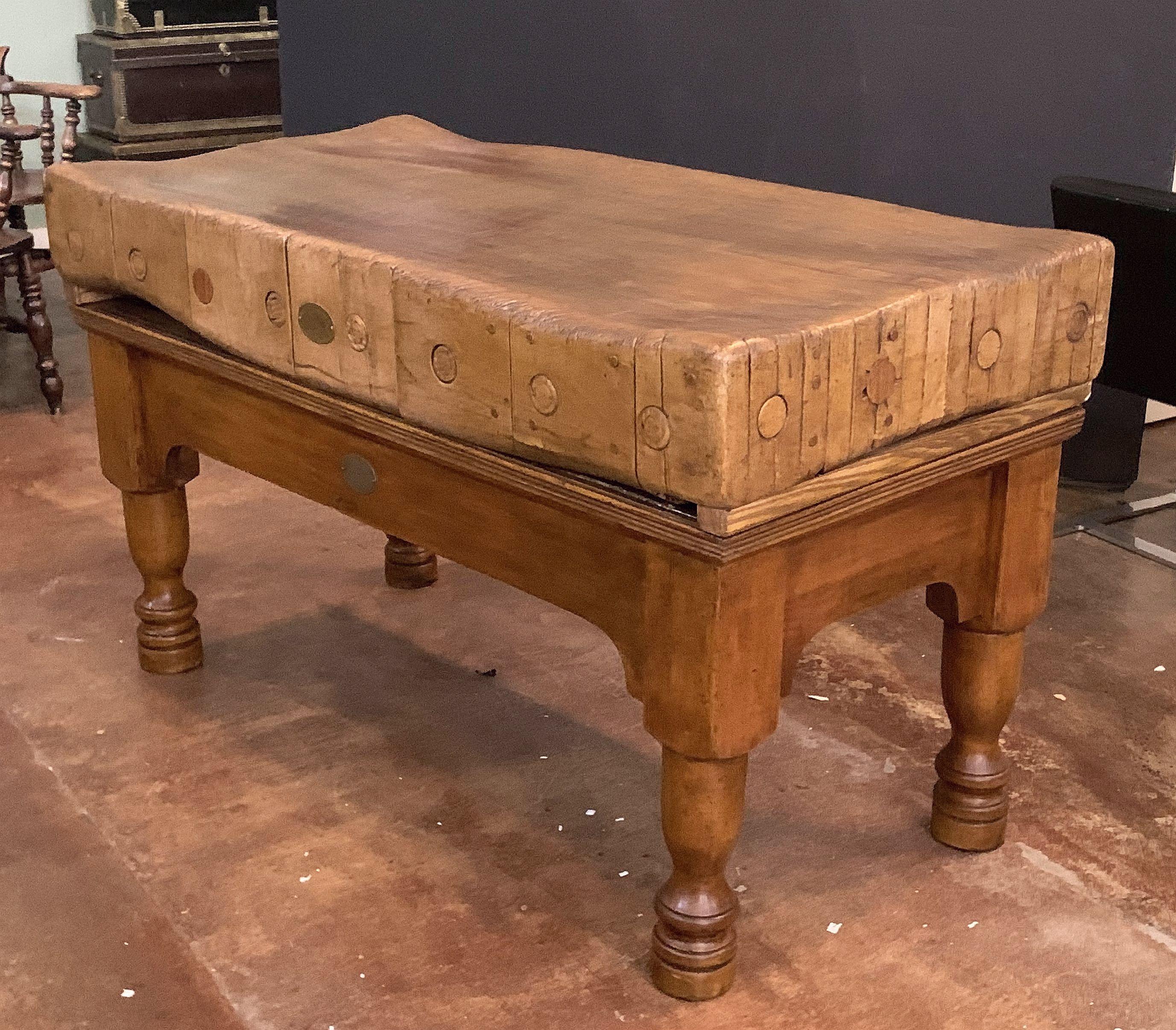 A handsome large English butcher's chopping block table, featuring a large, rectangular block or slab of wood set upon a bottom tier four-legged support stand. Ships in two pieces.

Oval brass medallion: William Douglas & Sons, Ltd., Putney,