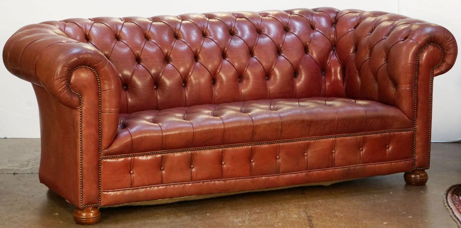A fine, large vintage English Chesterfield sofa upholstered in original patinated cordovan pale red-brown soft hide leather - featuring a deep button-tufted back, scroll arms, and comfortable seat, with matching buttoned valance to the front, the