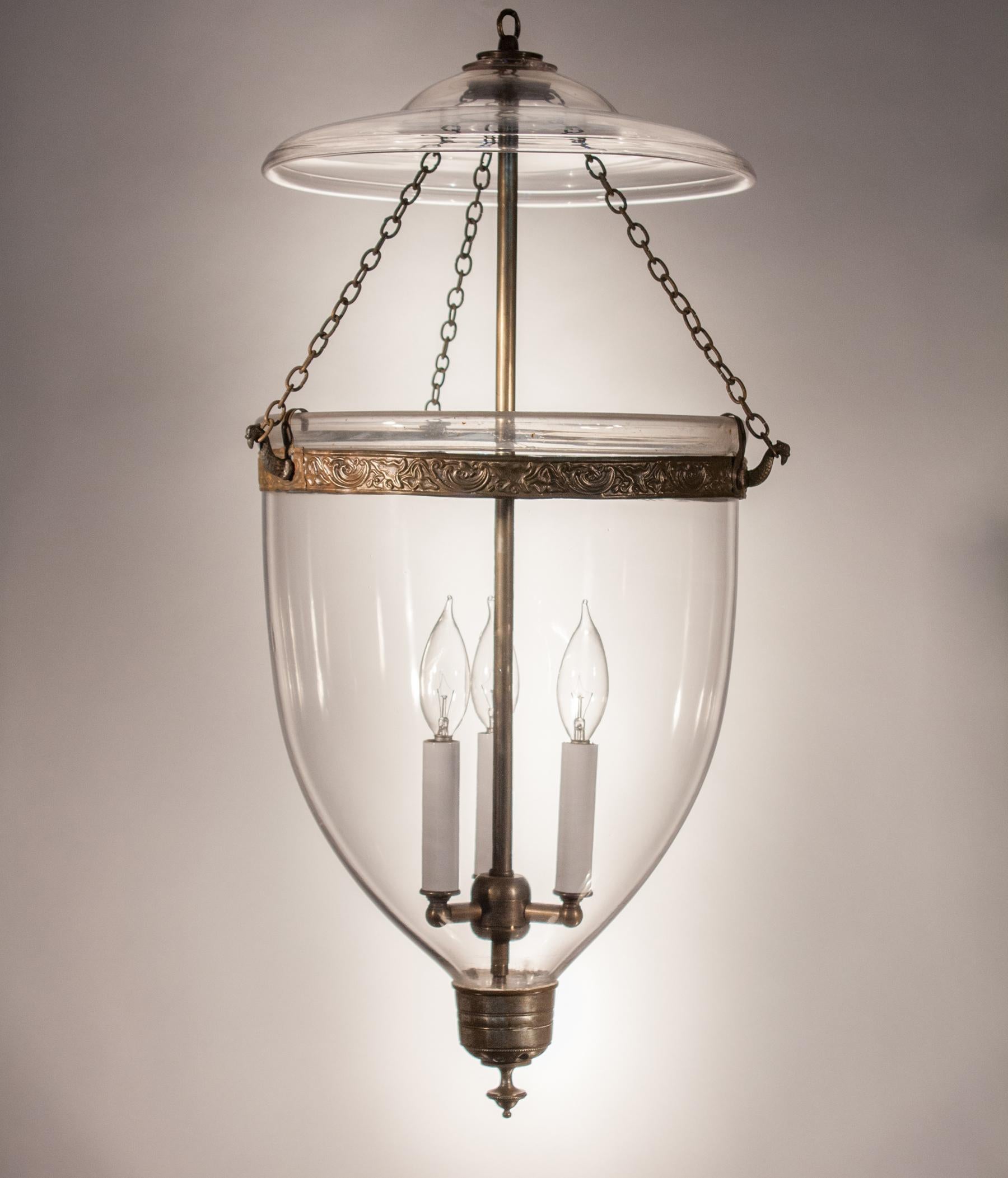 Simple and elegant, this larger-sized handblown clear glass bell jar lantern has a very pleasing form. The embossed brass band (which has been replaced for safety) and silver-toned finial add the perfect adornment to this pendant. The light has been