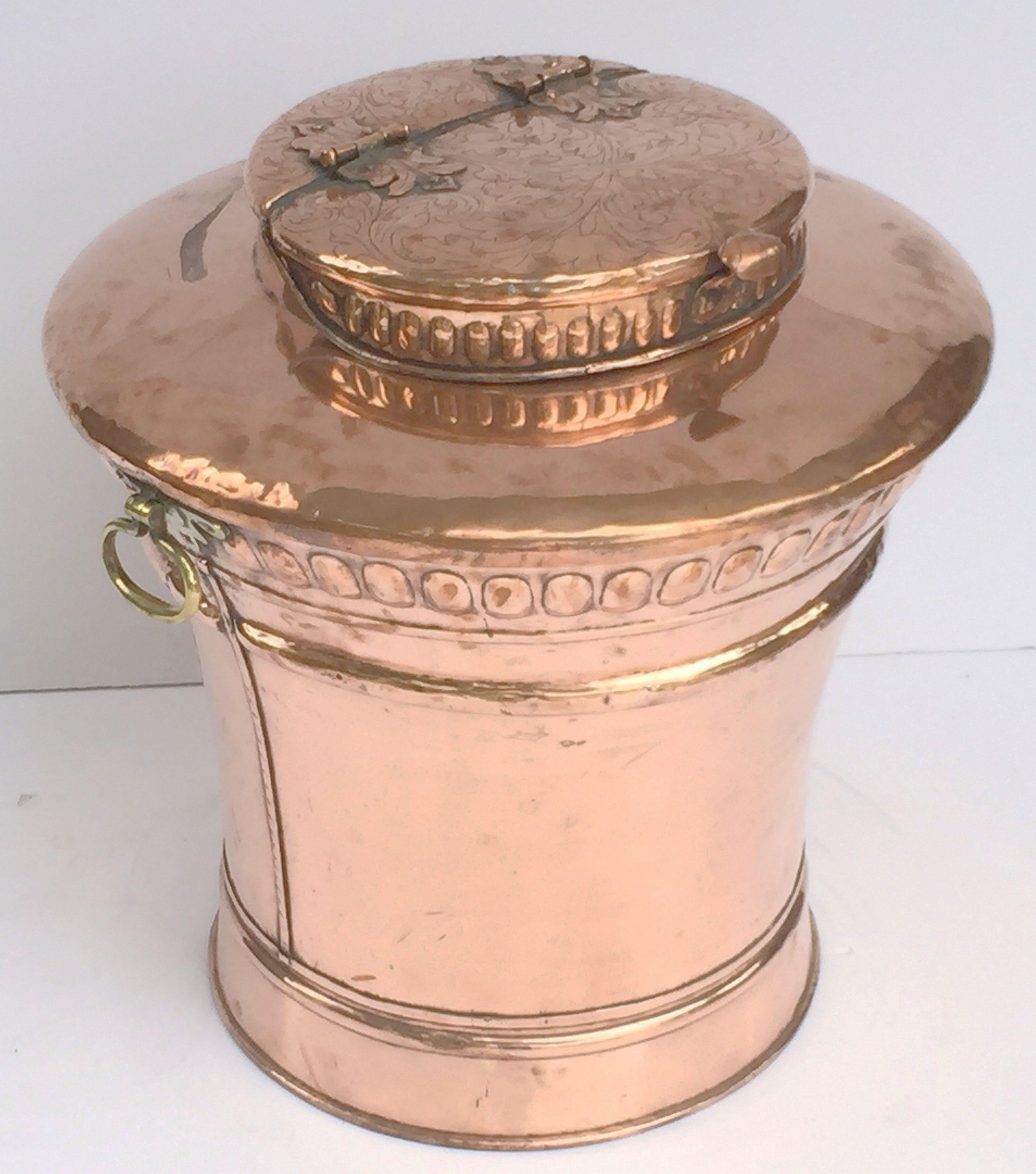 Grande urne ou corbeille anglaise en cuivre, dotée d'un couvercle à charnière surélevé avec un motif décoratif en relief, monté sur un corps circulaire avec des poignées en laiton opposées.

Mesures : Hauteur 29 1/2