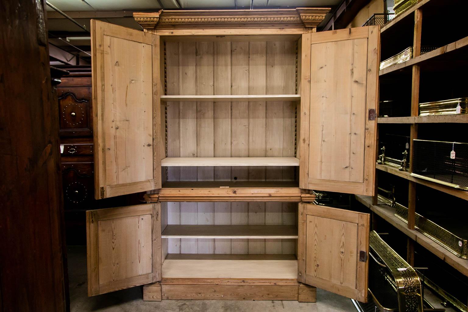 This cupboard is made from antique reclaimed pine. It has carved moldings on the cornice and stiles. There are two recessed molded panels on the top and bottom sides. The interior in the top has two adjustable shelves. The lower section has one