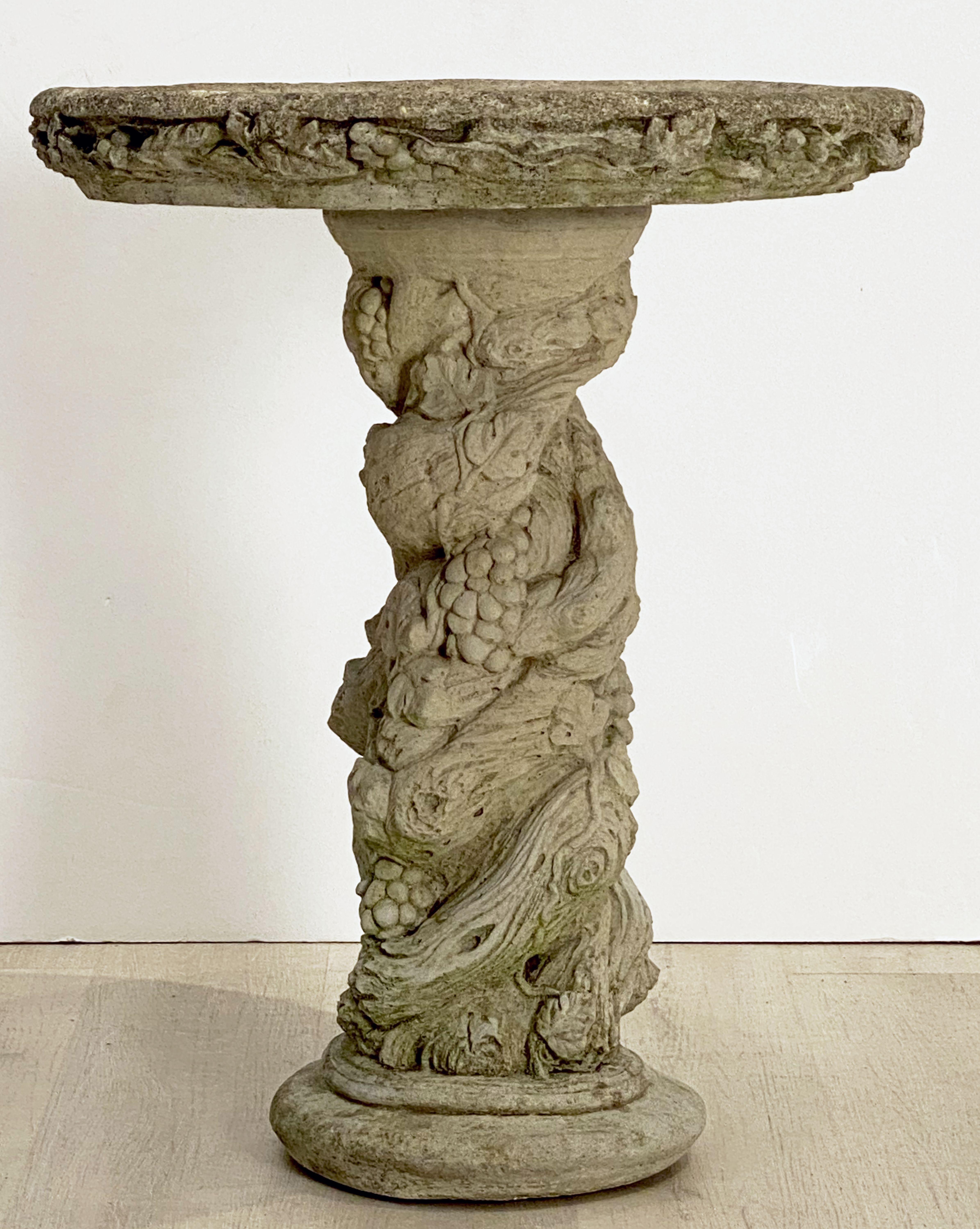 A handsome English bird bath (or birdbath) of composition stone, featuring a 22 3/4 inch diameter basin top (circular) with a faux bois design around the circumference, over a column pedestal with a fanciful faux bois relief, on a raised round