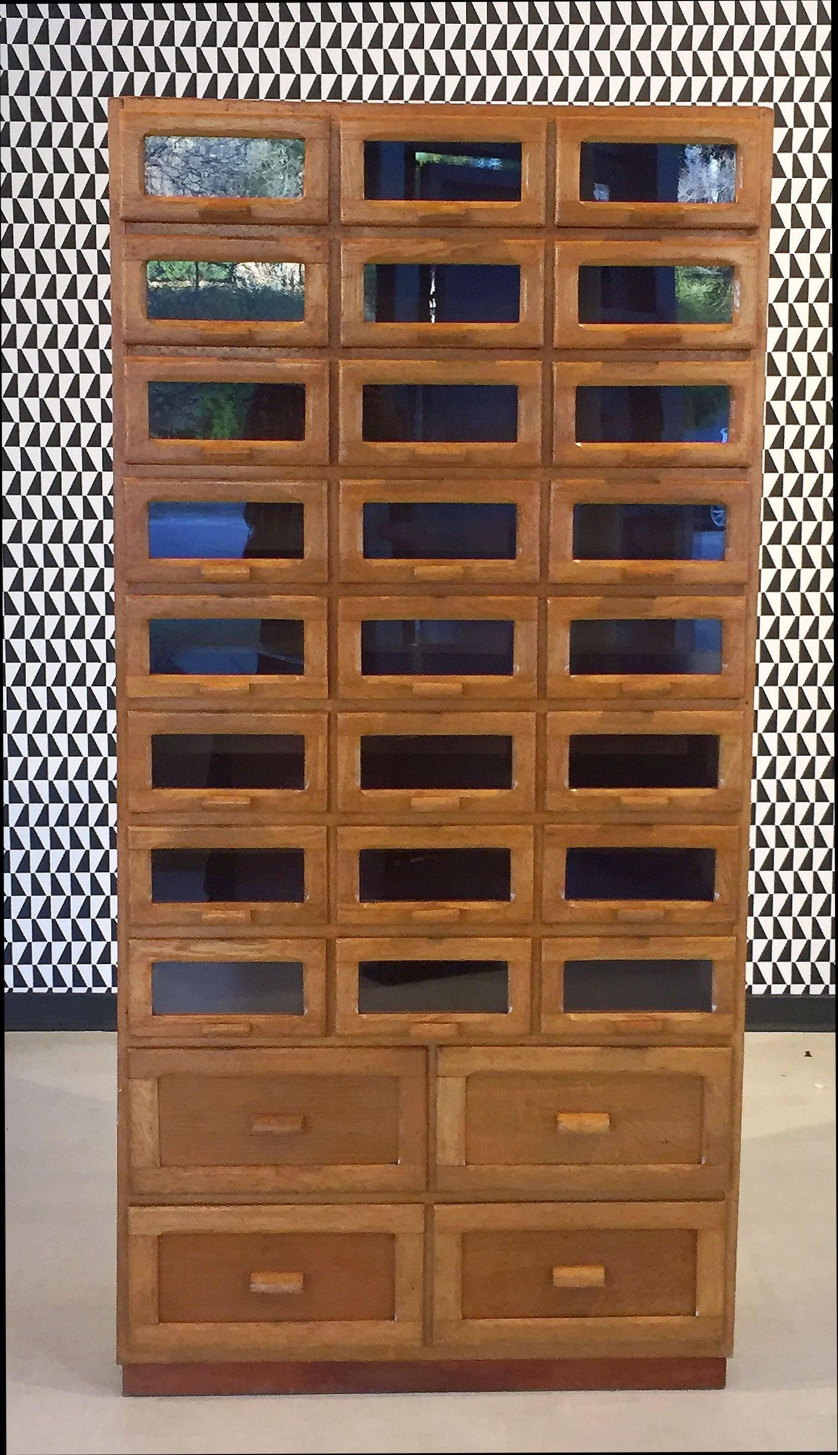 An exceptional large vintage haberdashery or haberdasher's cabinet from England featuring:

(24) glass-fronted drawers over four cupboard style drawers - (28) drawers total.

The fitted drawers with wooden pulls and set upon a raised