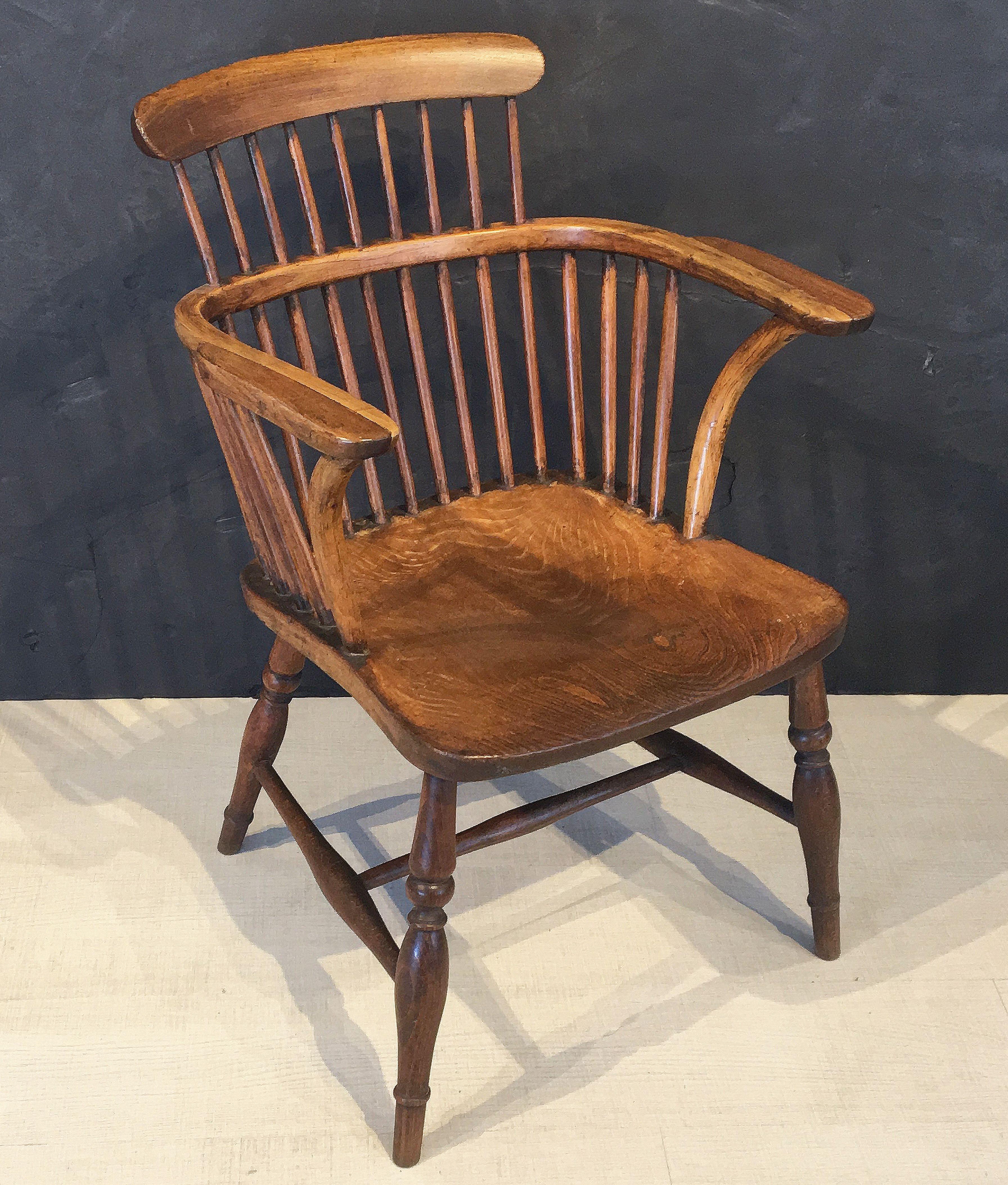 A handsome large English windsor smoker's armchair of elm and ashwood, featuring a high-back top rail and spindle back with bowed arm rail, with solid, comfortable seat on turned-leg stretcher base.