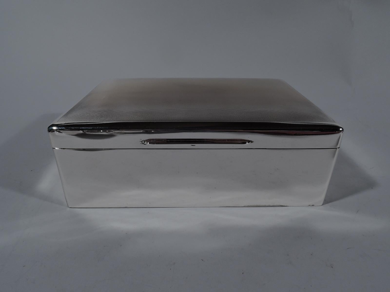 Large English modern sterling silver box, 1945. Rectangular with straight sides and curved corners. Cover hinged with gently curved and engine-turned top, and chamfered tab. Box and cover interior cedar-lined and partitioned. Box underside leather