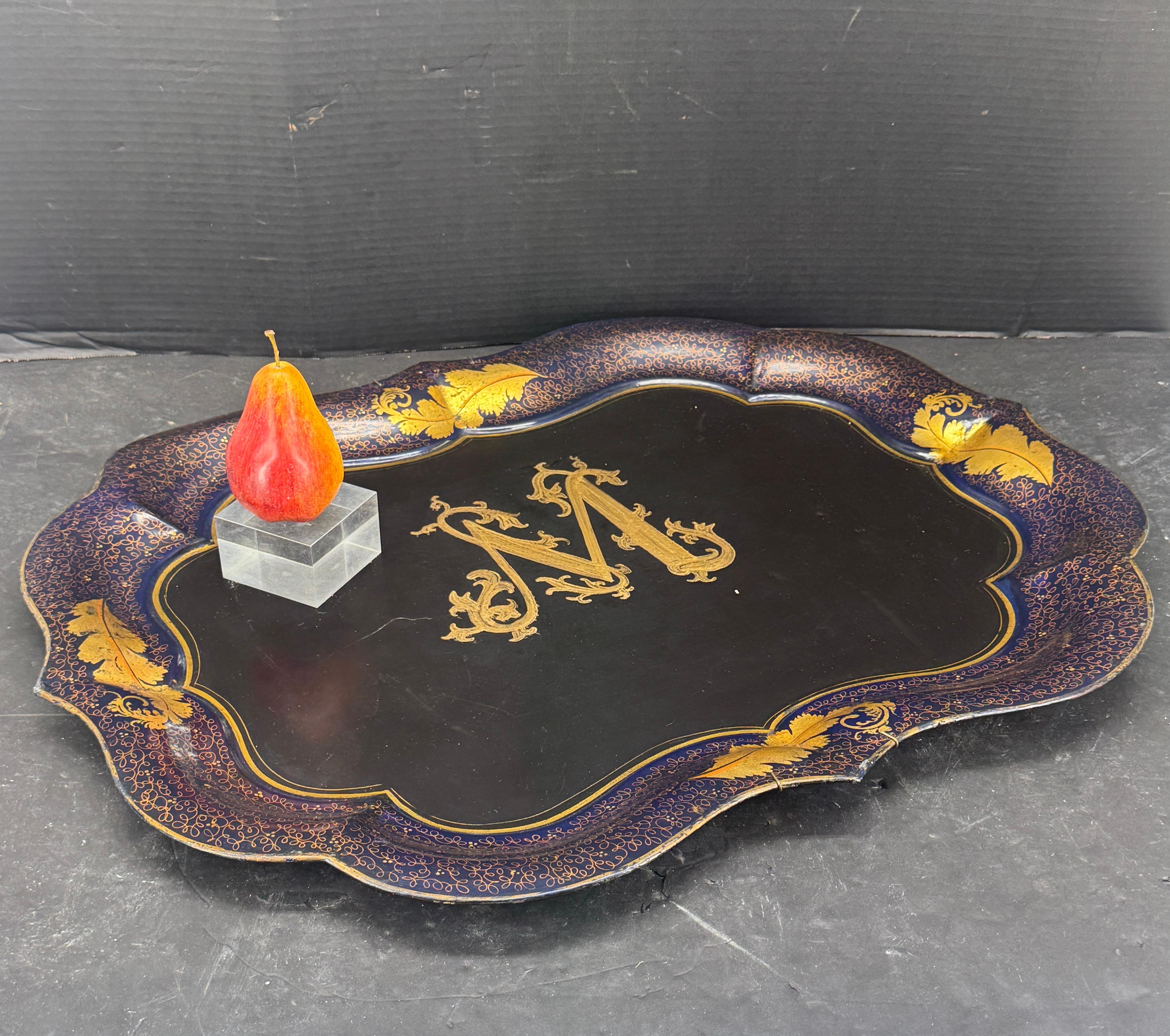 Unbeatable character on this black painted gilt tray. The tray features a floral pattern around the edges with a large monogram M in the center. We see this metal tray with dual purposes, can function on a coffee table, on top of an ottoman or on a