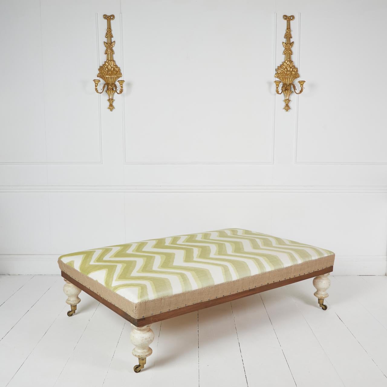 Traditionally upholstered coach-built ottoman stool standing on painted gessoed antique turned legs and period brass castors.
Covered in hand-loomed ikat aloe green Chevron bar 100% silk fabric by Bruschwig & fils. Top stitched natural hessian