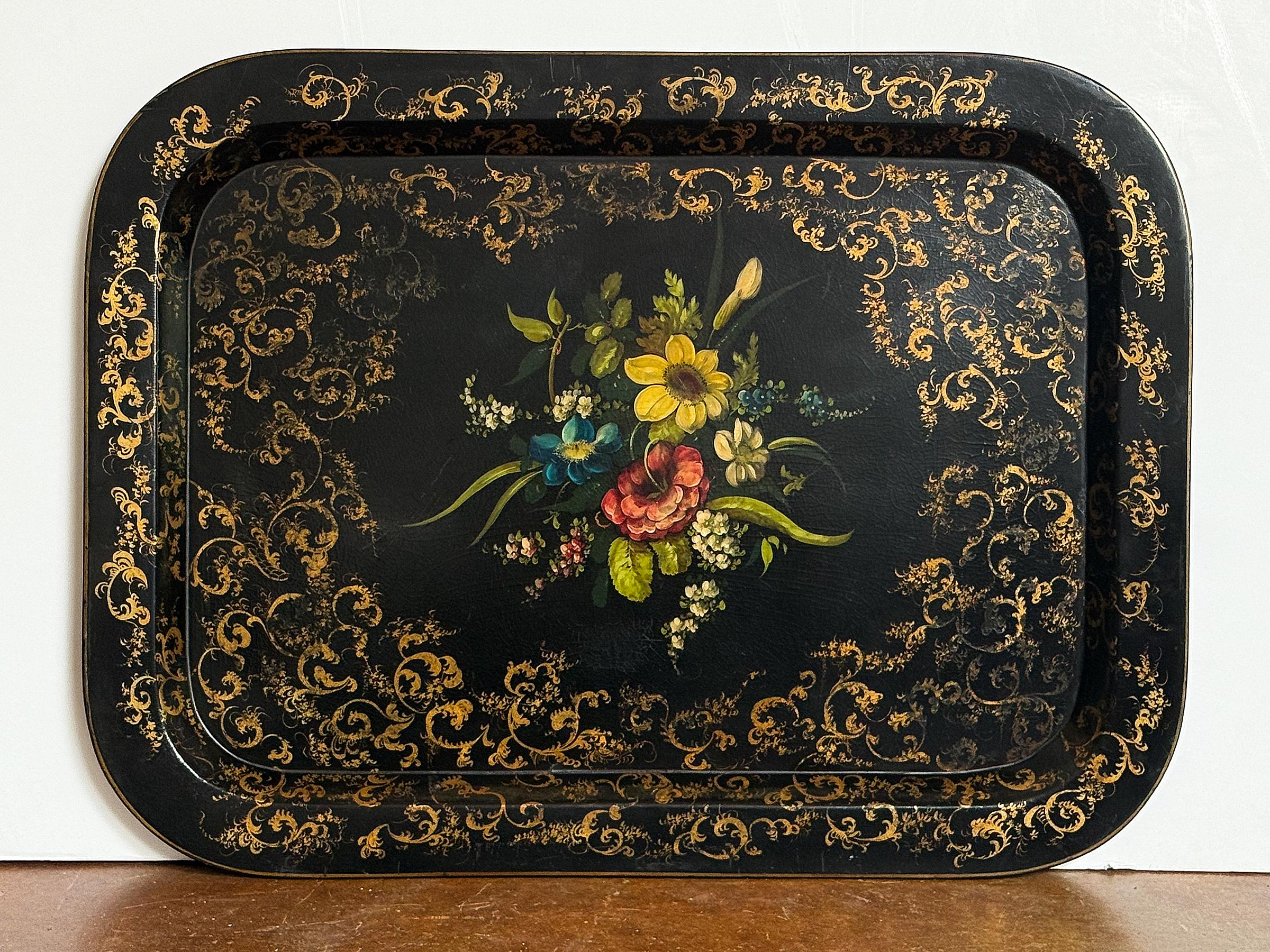 Un grand plateau anglais en papier mâché laqué noir de la période du Mouvement Esthétique, présentant une peinture décorative de fleurs et des volutes rococo dorées. 

Mesures : H 20 in x L 26 5/8 in