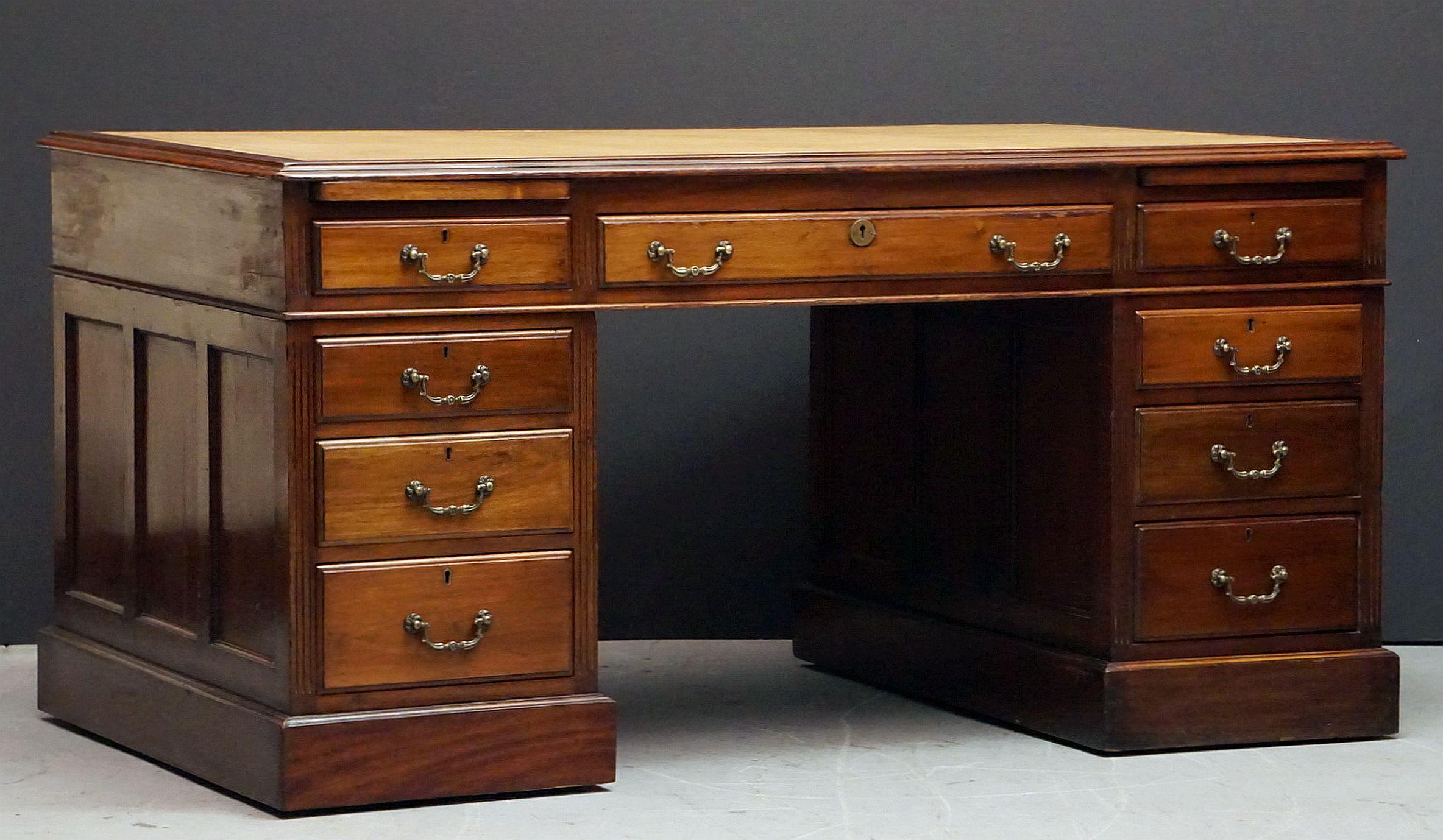 A handsome large English partner's desk of mahogany, featuring a moulded top inset with an embossed cream leather, over a frieze with one long drawer flanked by two short drawers, with two pull-out slides above each short drawer. 
Resting on two