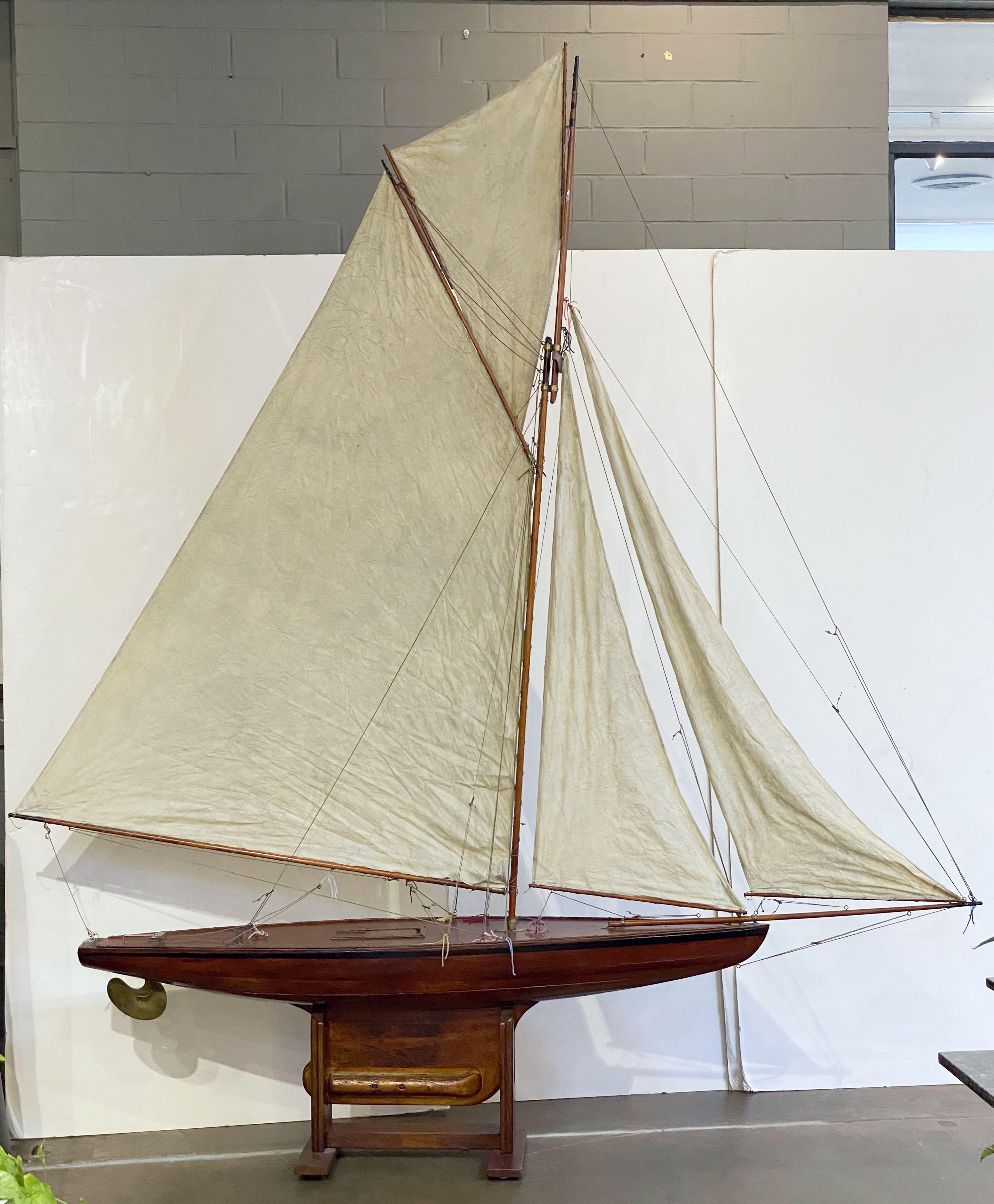 A very large scale handsome English pond yacht (over nine feet high), handcrafted from wood and brass and featuring vintage cloth sails and fittings.

Displayed on a separate, custom-fitted stand.

Height and depth includes the