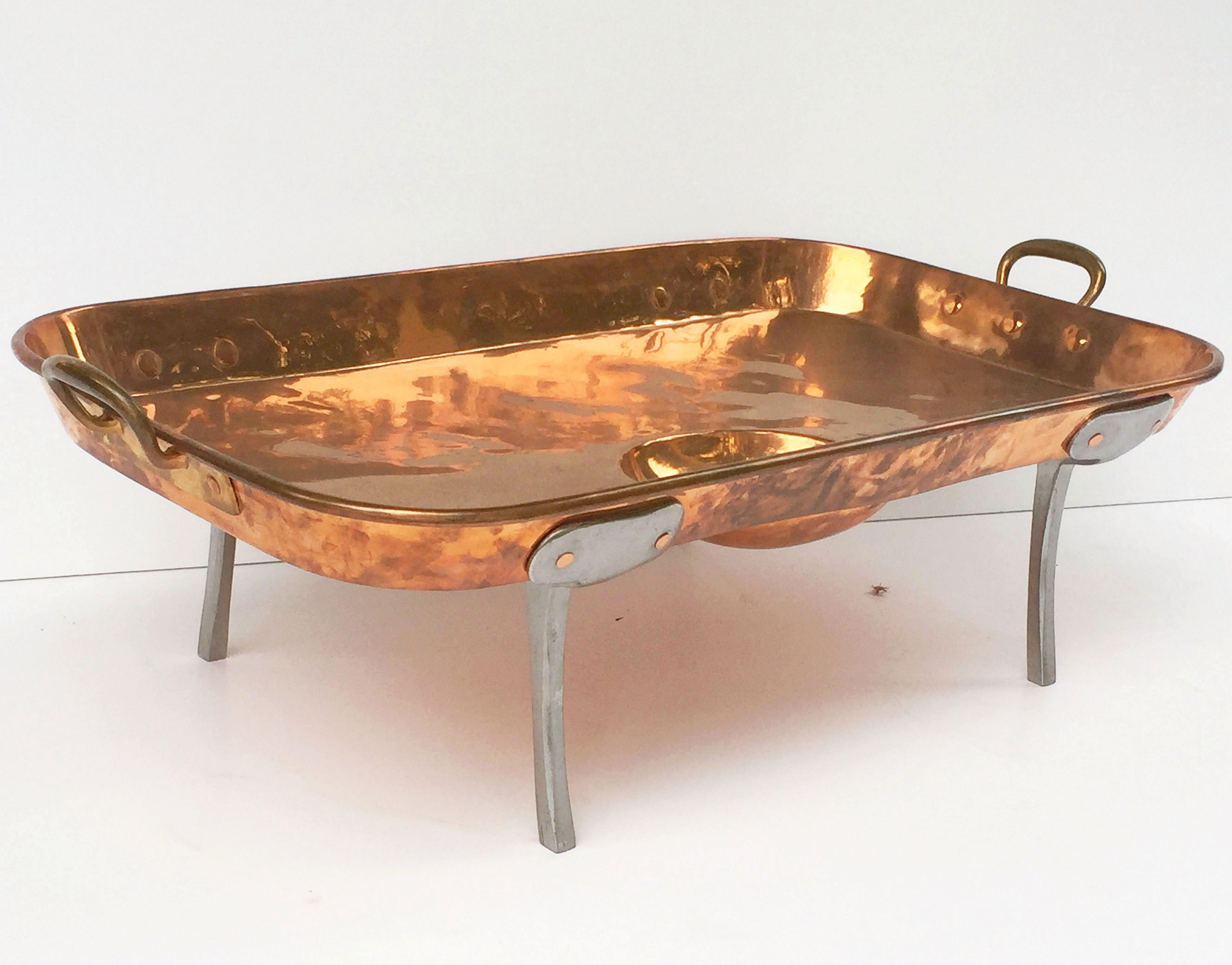 A handsome large English rectangular copper serving tray or platter with a well and two opposing handles, resting on four steel feet.