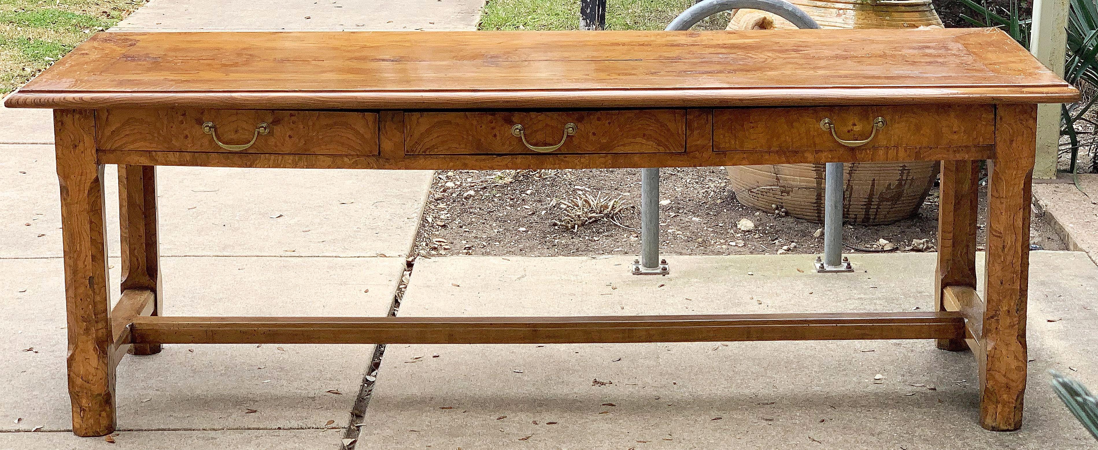 A large English trestle (or farm) table of burled or burr ash featuring a lovely paneled rectangular top on a trestle support frame with three drawers on one side, each drawer with brass pull, and standing on handsome chamfered square