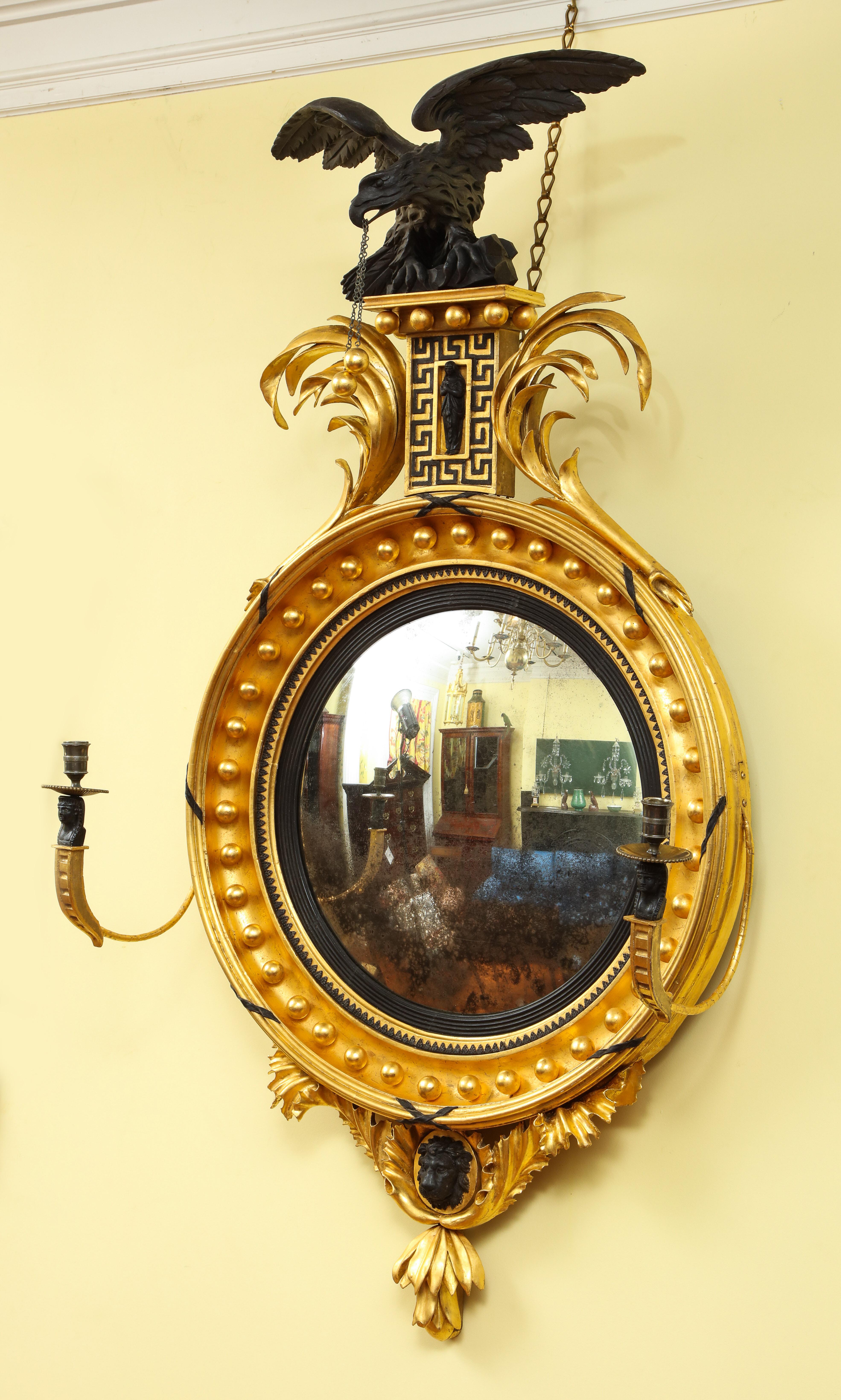 Fine Regency giltwood and ebonized convex mirror in the Egyptian taste, having an ebonized spread winged carved eagle surmount with gilt balls and chain suspended from its beak, on a raised central gilt plinth having applied meandering Greek key