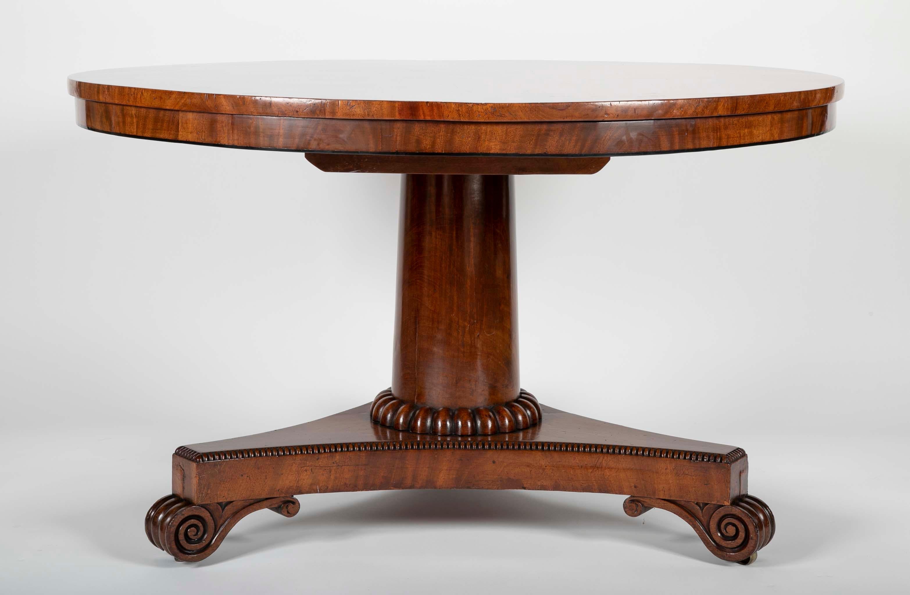 A crotch mahogany English Regency tilt-top table. The top rising on an unadorned single column from a gadrooned tripartite base raised on scroll feet.