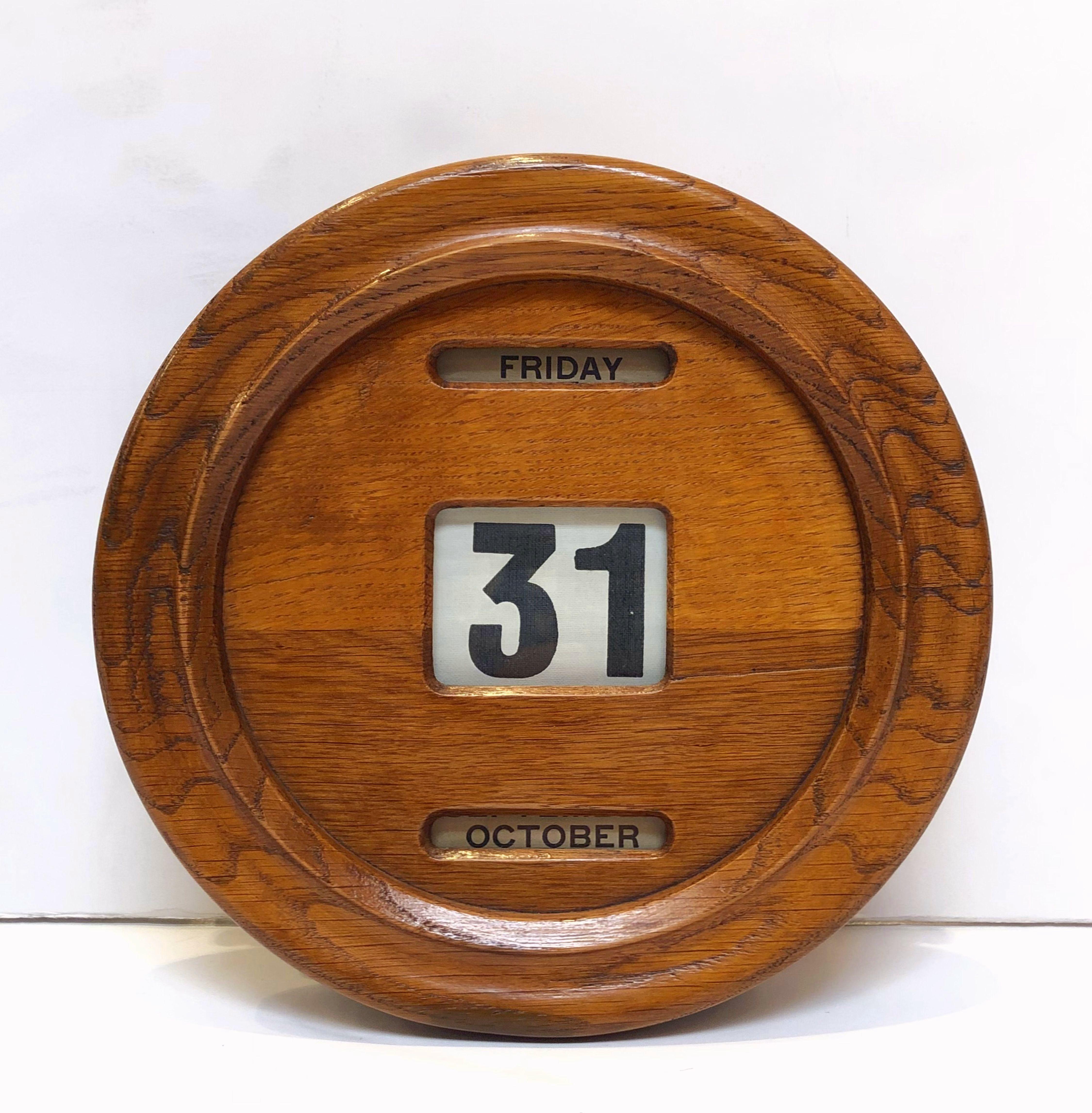 A fine large English perpetual calendar of patinated oak from the Edwardian era, featuring with a round face-plate (diameter 9 inches) mounted to a box back, with original fabric spools behind glazed panels, the four adjusters on each side present