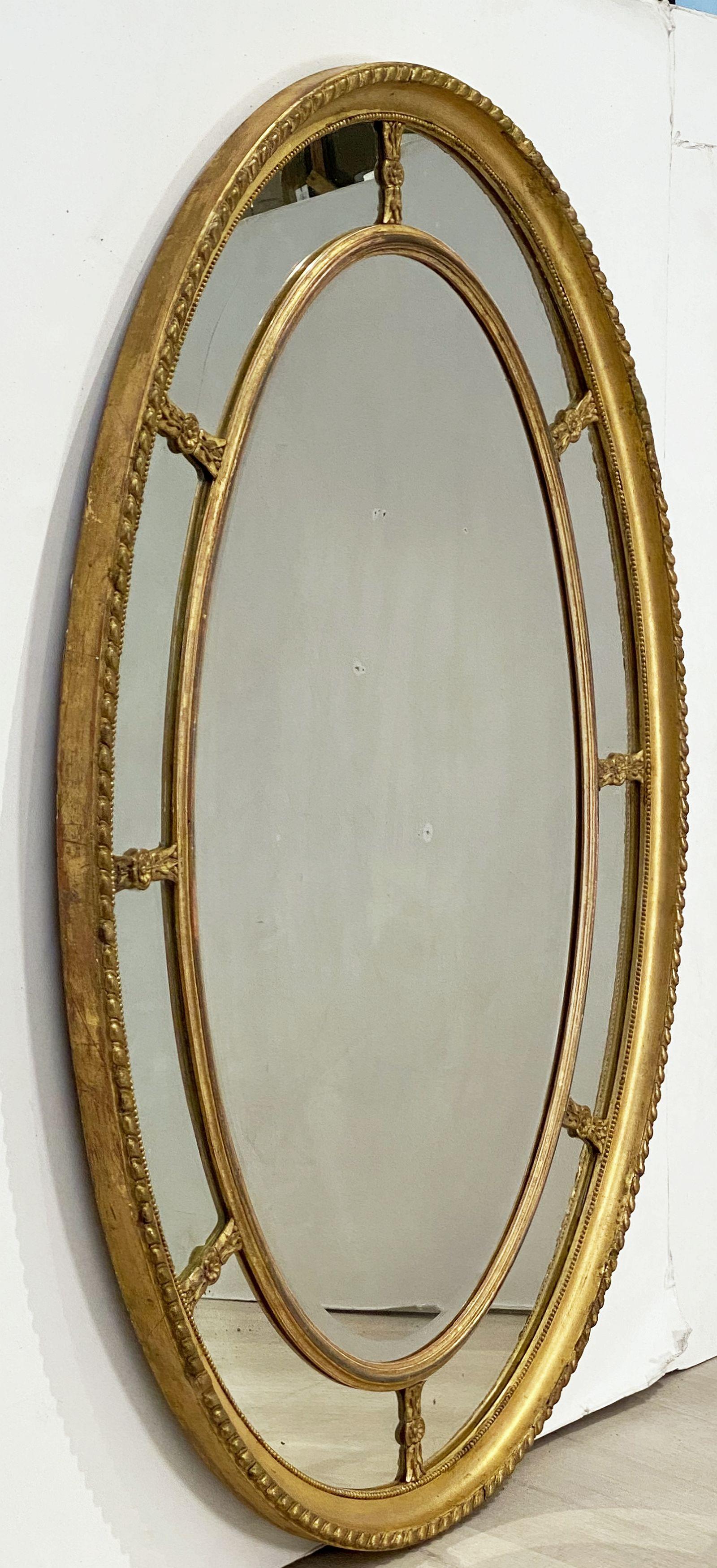 A handsome large English segmented gilt oval wall mirror in the Adam style, featuring a gilt wood oval segmented marginal border mirror. 
The carved, rope-edged frame showing eight small inner mirrors with eight leaf and flower head divides,