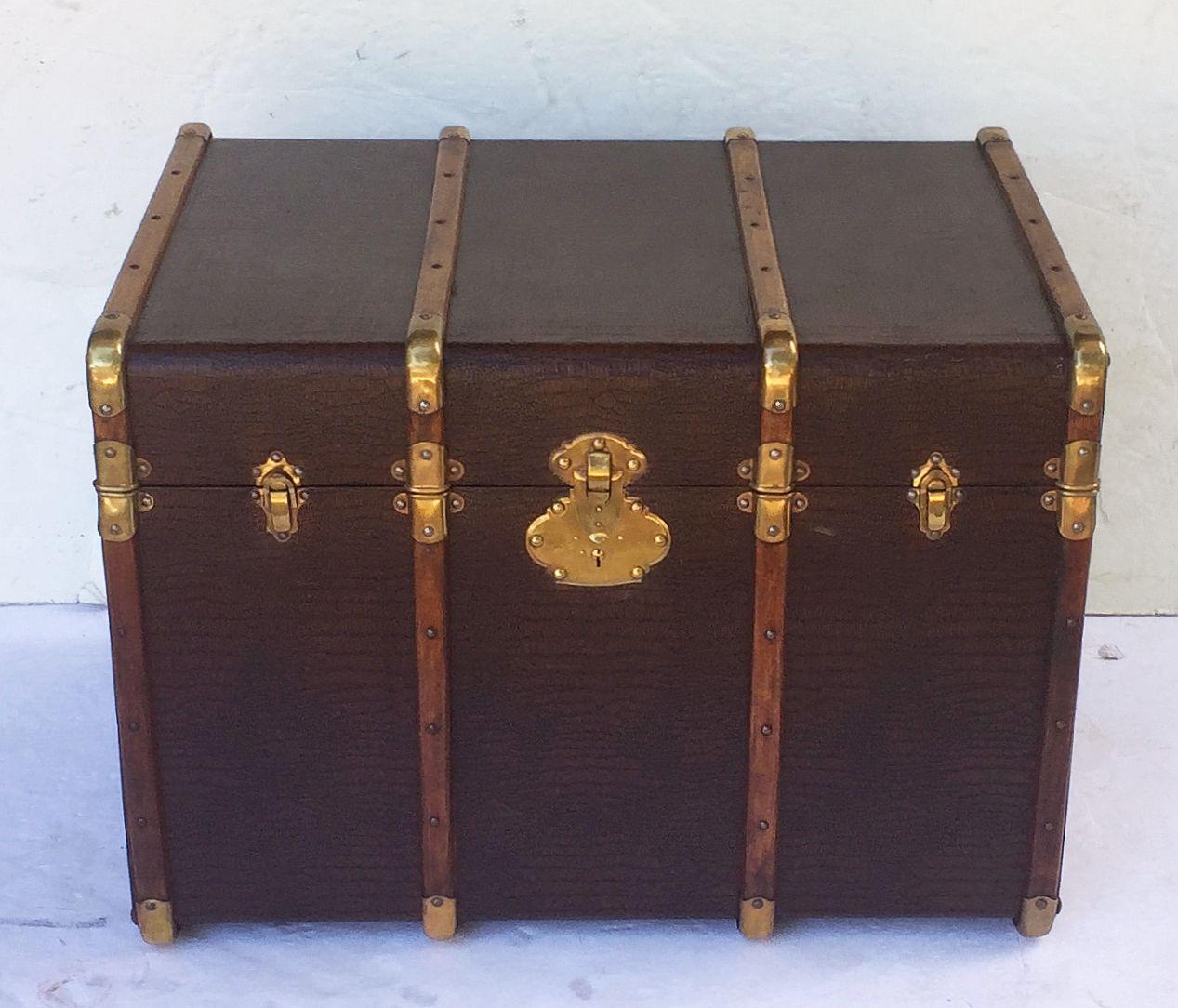 A handsome large English traveler's luggage or shipping trunk of brass-bound paneled wood, featuring an embossed faux leather covering, brass and leather hardware, and a lined patterned interior.
