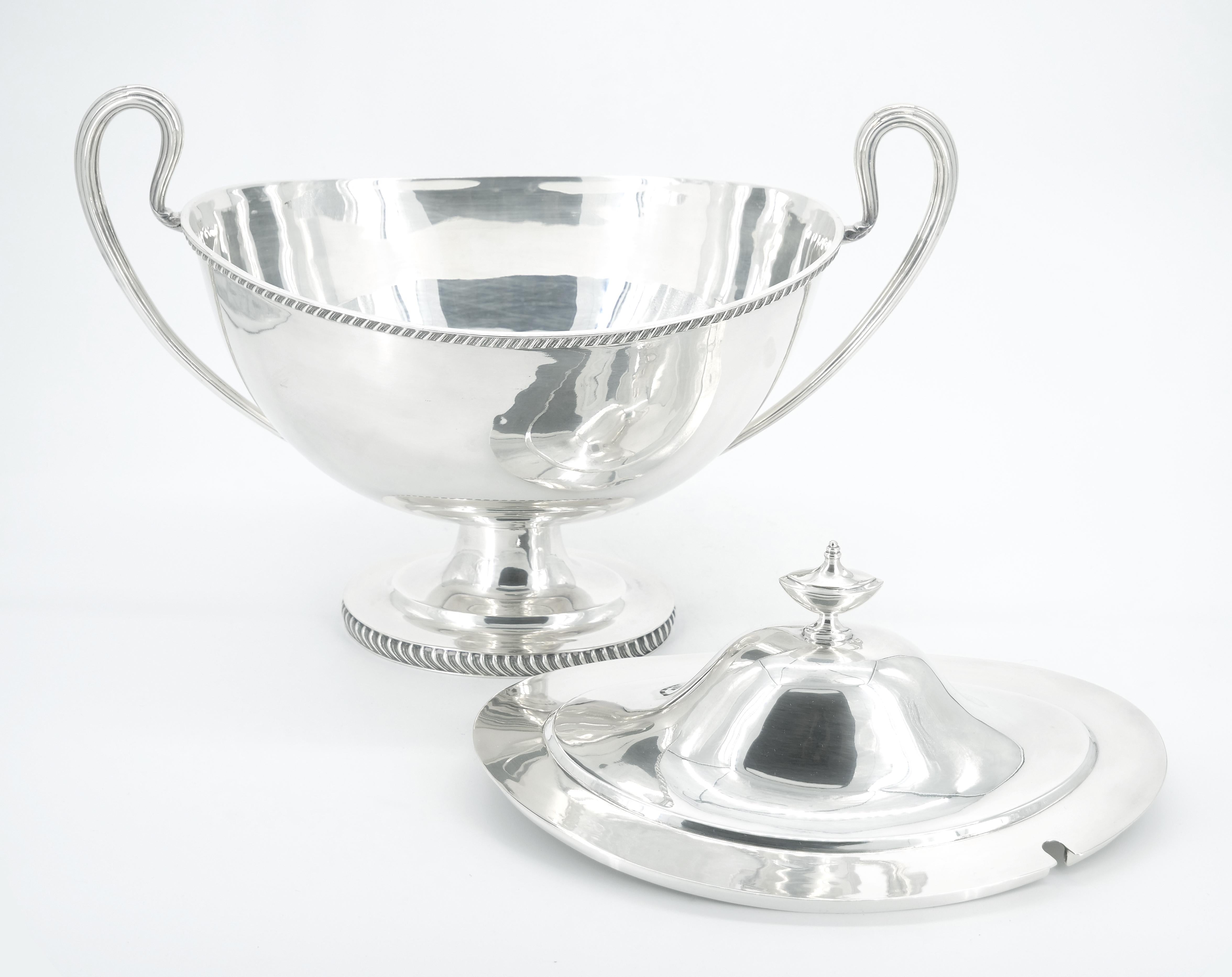 Immerse yourself in the refined elegance of our Large Early 20th Century English Silver Plate Tableware Covered Tureen. This striking piece boasts a sleek and clean Art Deco design, featuring a distinctive boat shape with two gracefully arched,