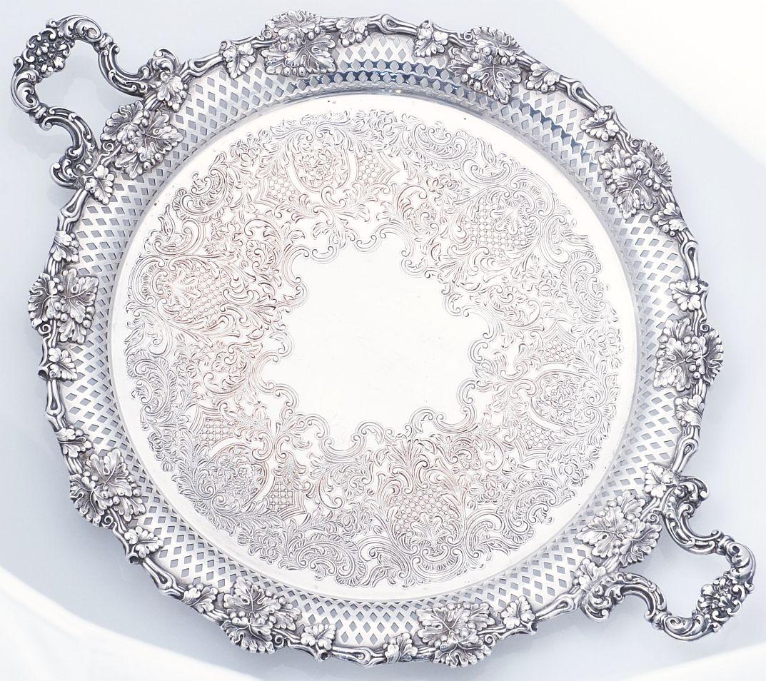 A handsome English round serving or drinks tray of fine Sheffield plate silver, featuring two opposing handles and a stylish pattern of grape clusters and leaves around the pierced circumference, with an etched scrollwork design in the center.

