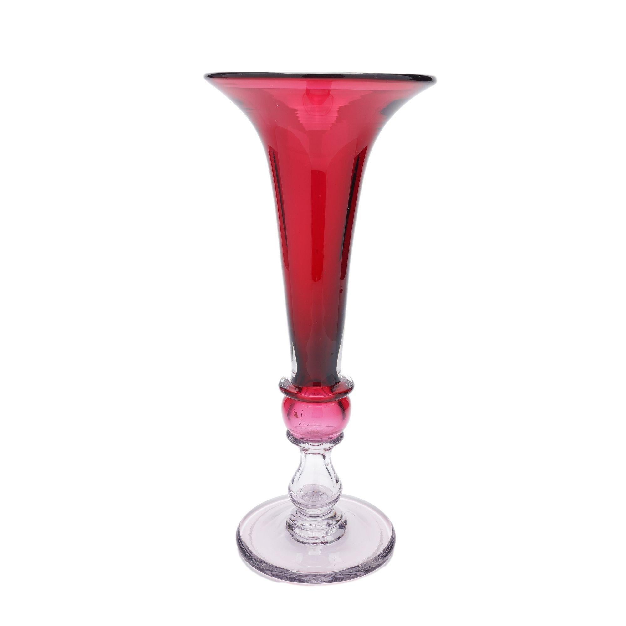 Vaso alto a tromba in vetro soffiato a mano di colore mirtillo rosso che poggia su un piede circolare trasparente con pontile molato e lucidato.
Inghilterra, seconda metà del XIX secolo.