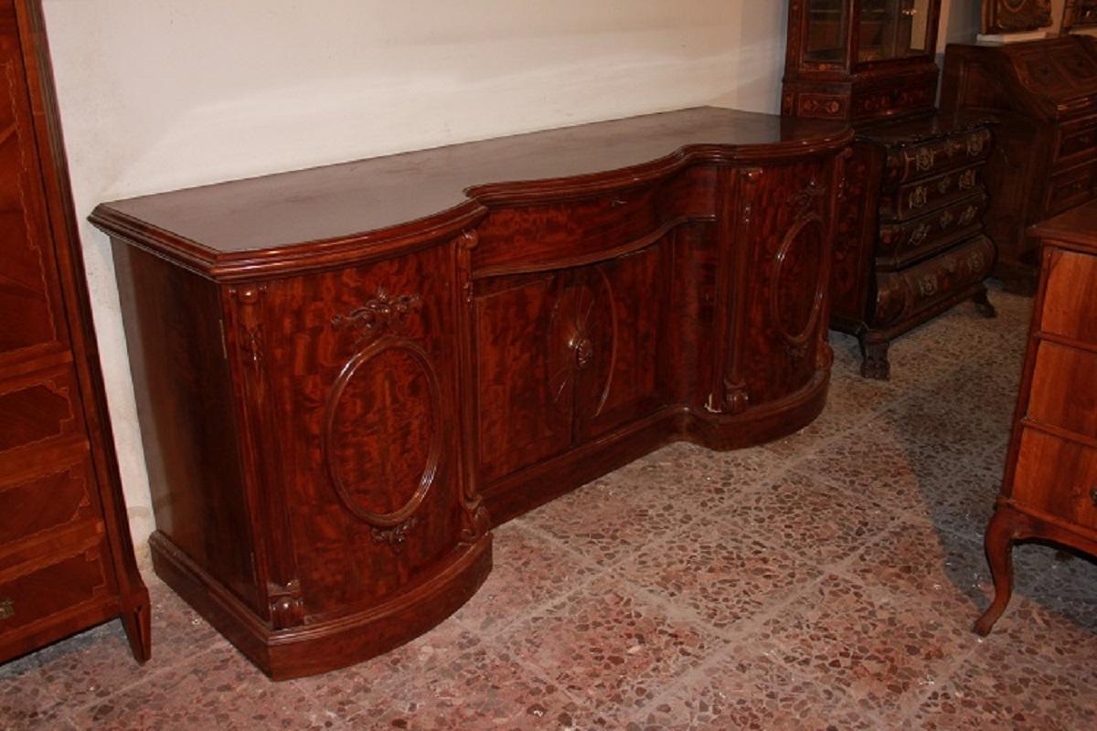Large English sideboard from the second half of the 1800s, Victorian style, in mahogany wood. It features 2 side doors, 2 central doors, and 1 large drawer below; all embellished with carved motifs on the doors and side columns. Internally, the
