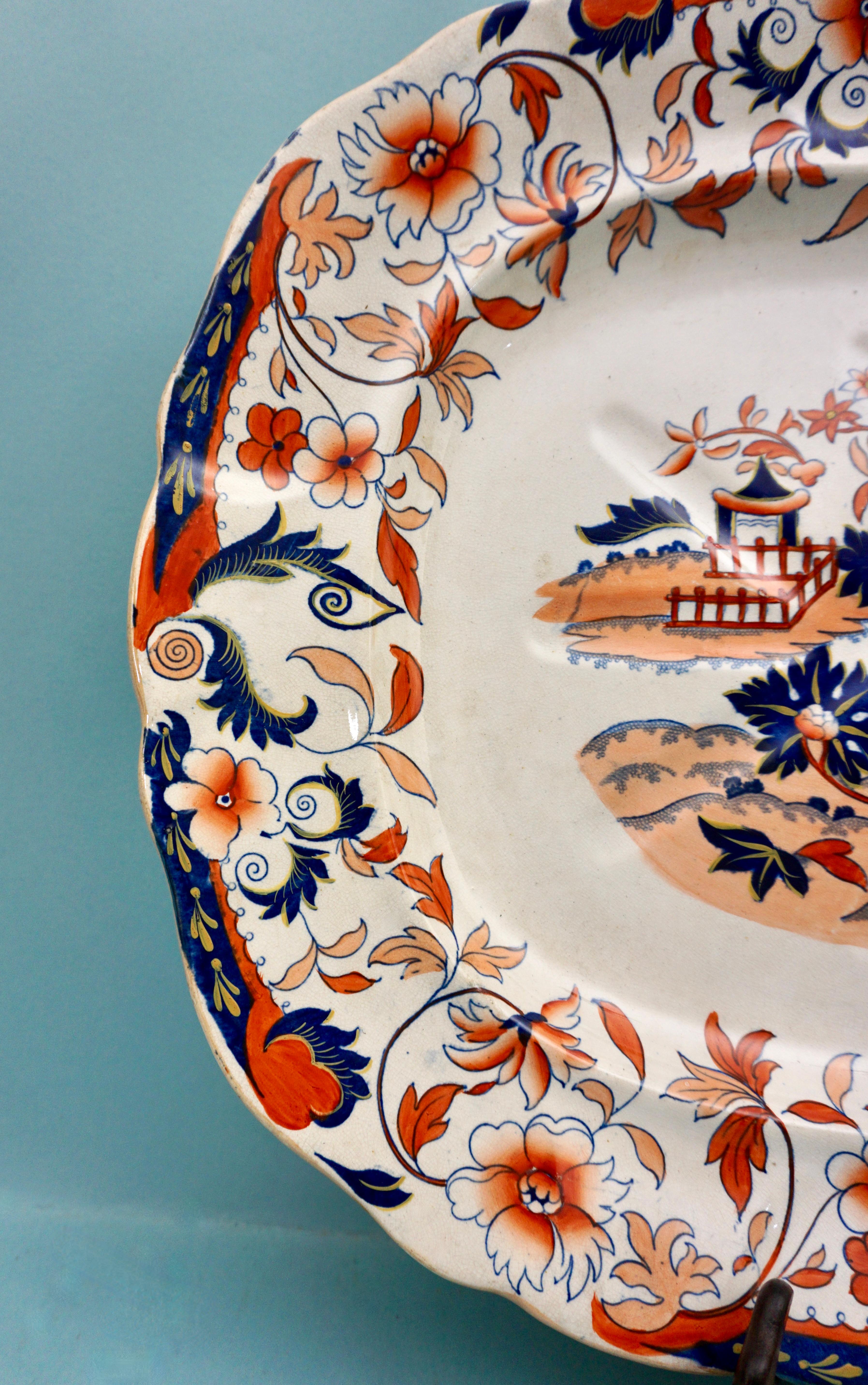 An attractive English Victorian period large scale well and tree platter decorated in the Asian taste with a central cartouche depicting a Chinese style structure in a stylized floral setting in tones of blue, red and ochre on a cream field. The