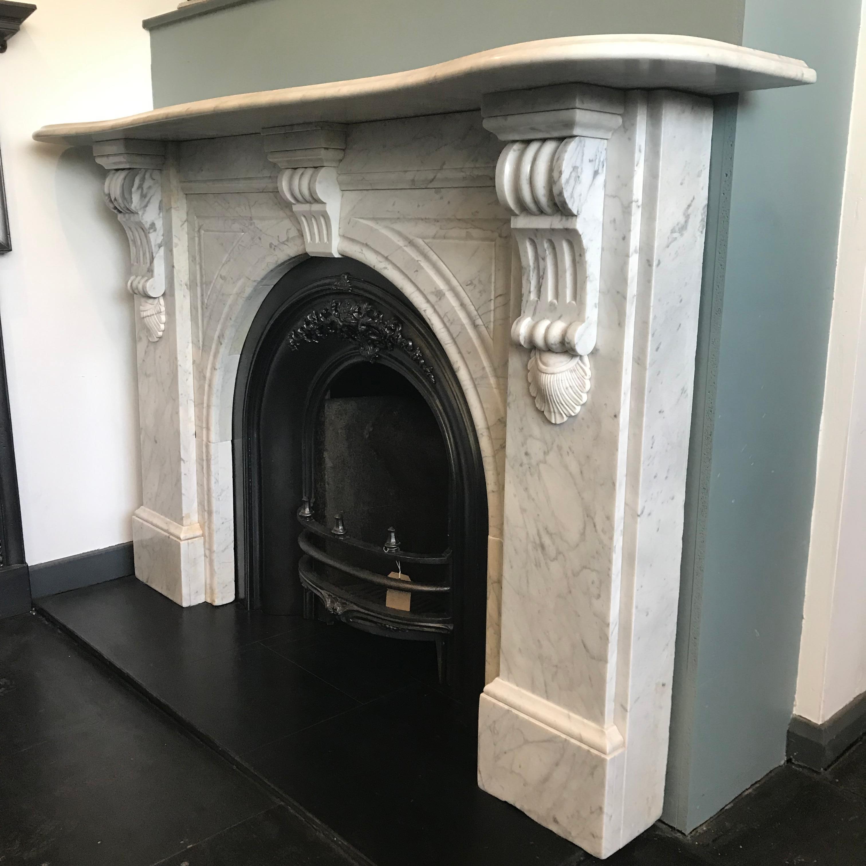 Large Victorian Carrara white marble fireplace surround with and arched aperture and heavily carved corbels supporting the serpentine shelf. Circa 1875.  Complete with an original Victorian cast iron arched grate.
