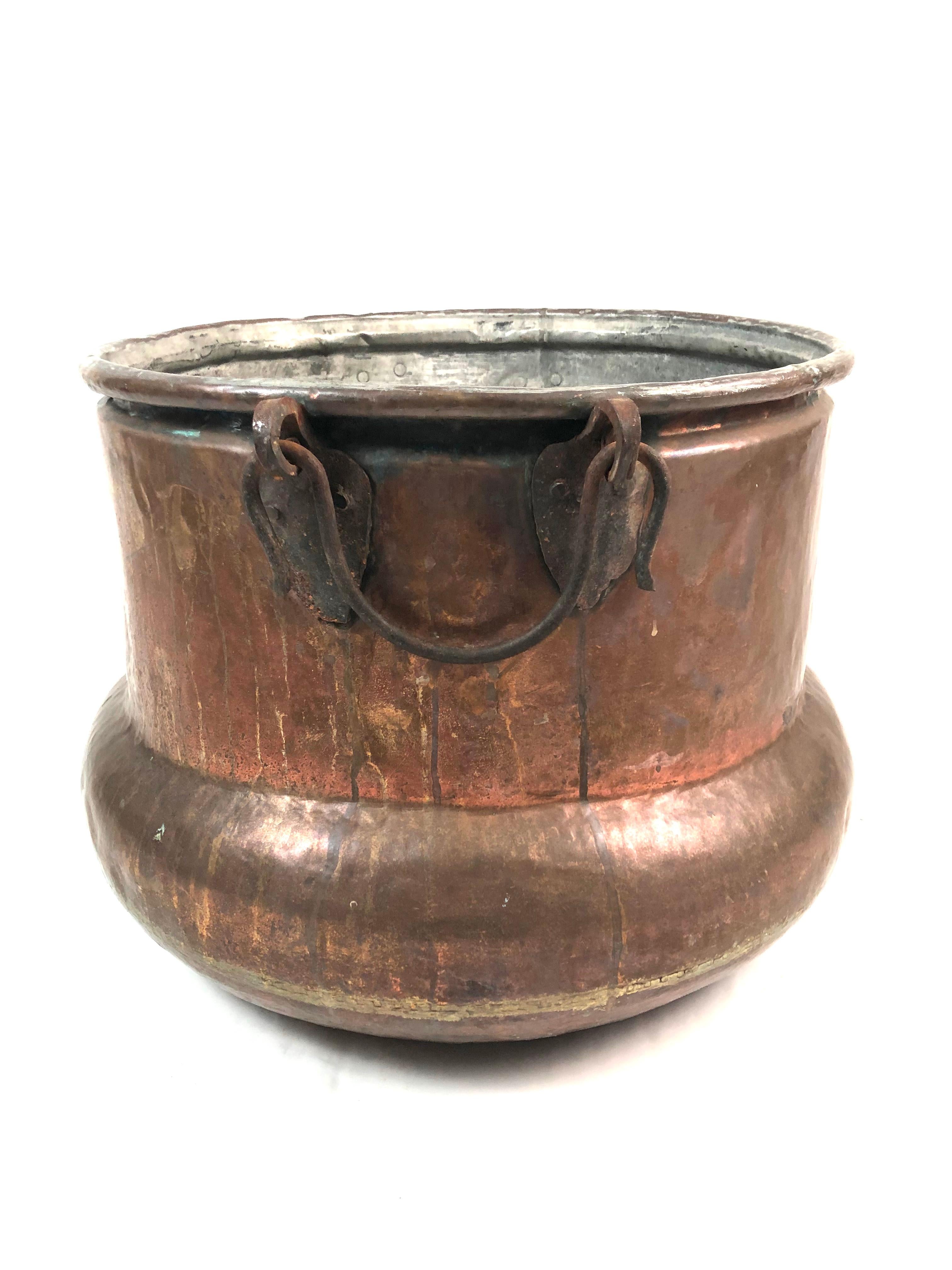 A large copper cauldron, or bucket, of circular form with larger lower section and 2 wrought iron carrying handles. Perfect for storing firewood.