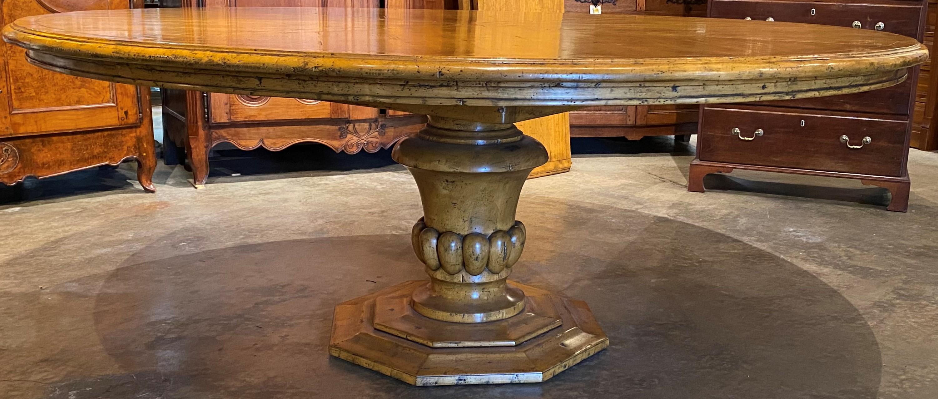 A beautifully carved large fruitwood round pedestal dining table in the European style with two leaves, on an decorative carved urn form octagonal base. When expanded with two leaves, there are two additional support legs inside that can be attached