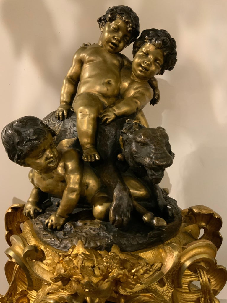 Gilt bronze Rococo sculpted base with floral and scrolls and a head of bacchaus at the center
Supports a sculpture after Charles Anfrie of three playful children riding a tiger. The sculpture
Is in a darker patinated bronze.