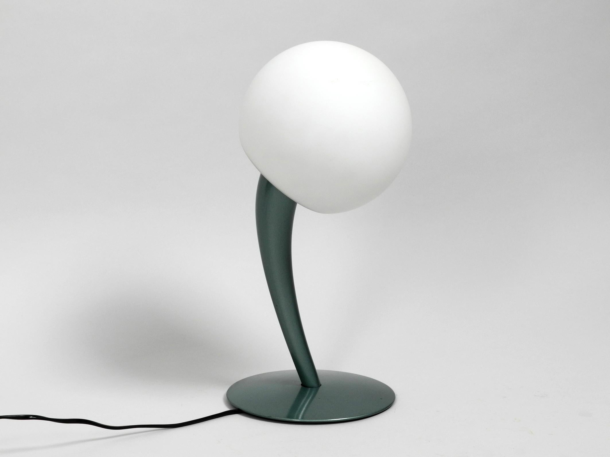 Great extraordinary table lamp from the 1980s or 1990s. Rare Minimalist design.
The lamp neck tends to the side, what gives the lamp an organic shape.
Frame is painted in typical 1980s blue green and is made entirely of metal.
Shade is made of