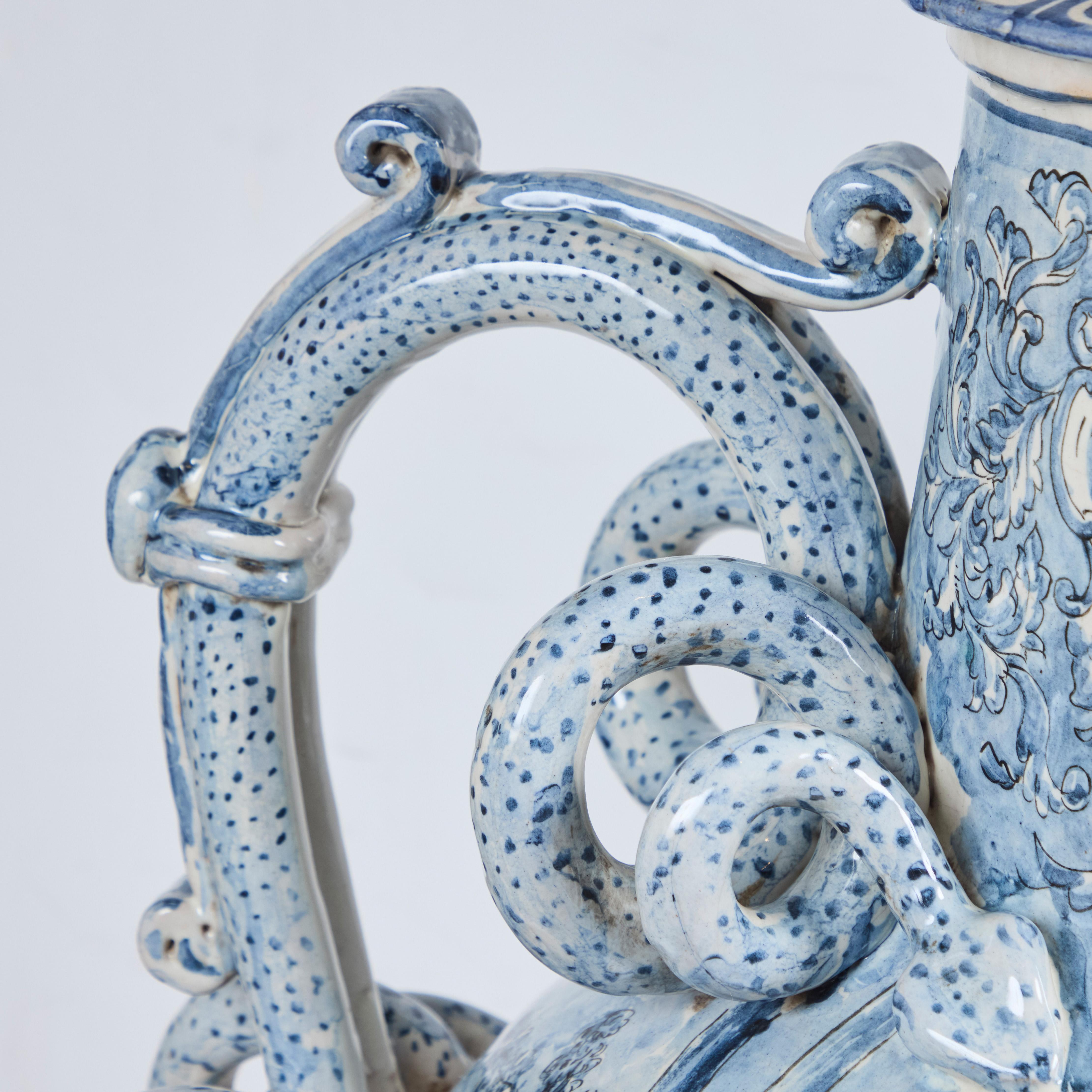 Grande brocca da vino rivestita in maiolica, decorata con figure danzanti, che festeggiano nel villaggio.  Le maniglie dei serpenti terminano con figure con volti sorridenti.  